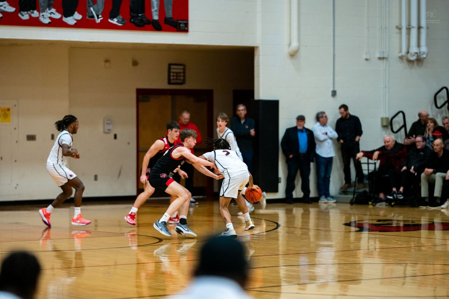 High school basketball players battle for position near half court during competitive indoor gymnasium game.