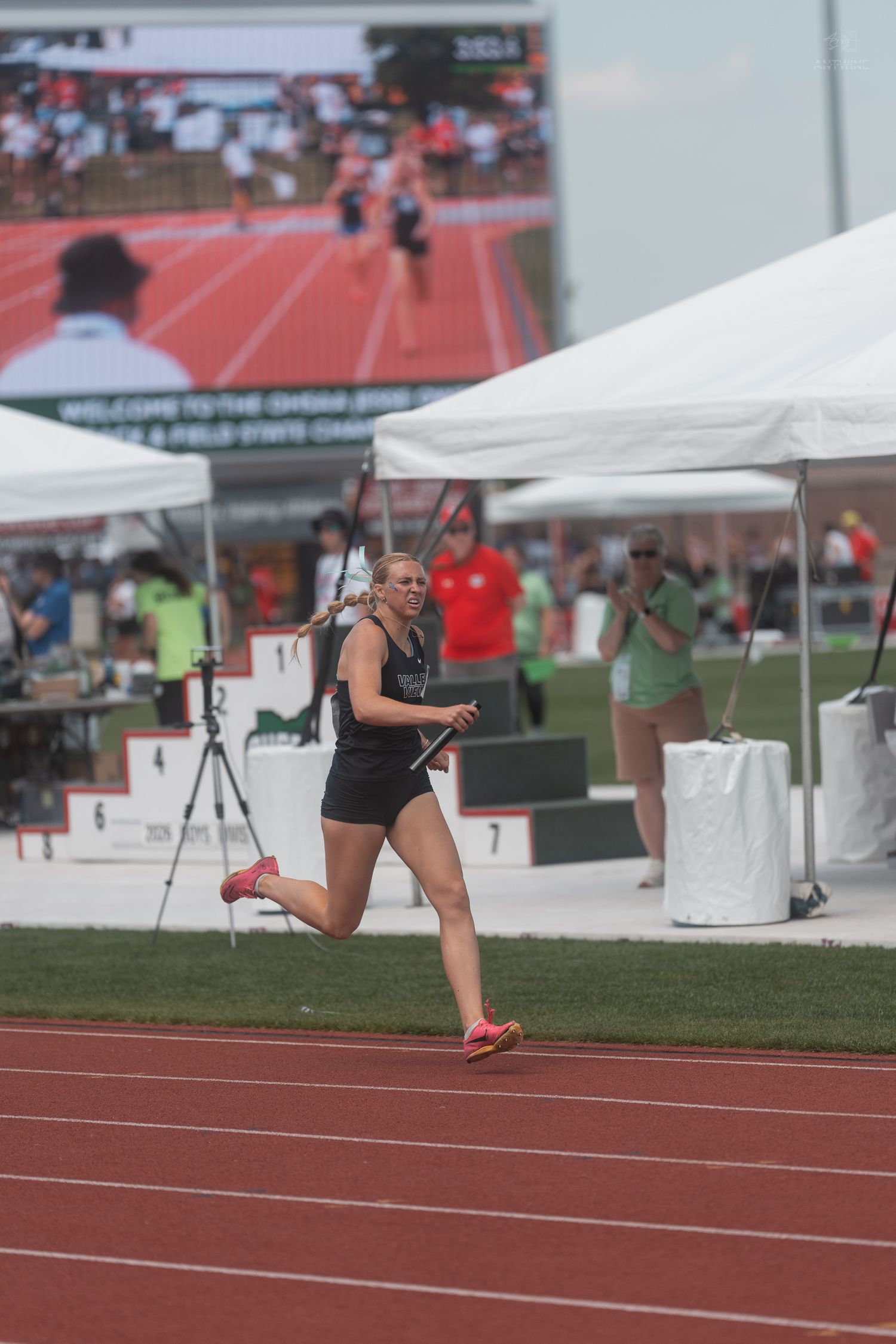 Female athlete sprints while holding a relay baton at the Ohio OHSAA State Track and Field Championship.