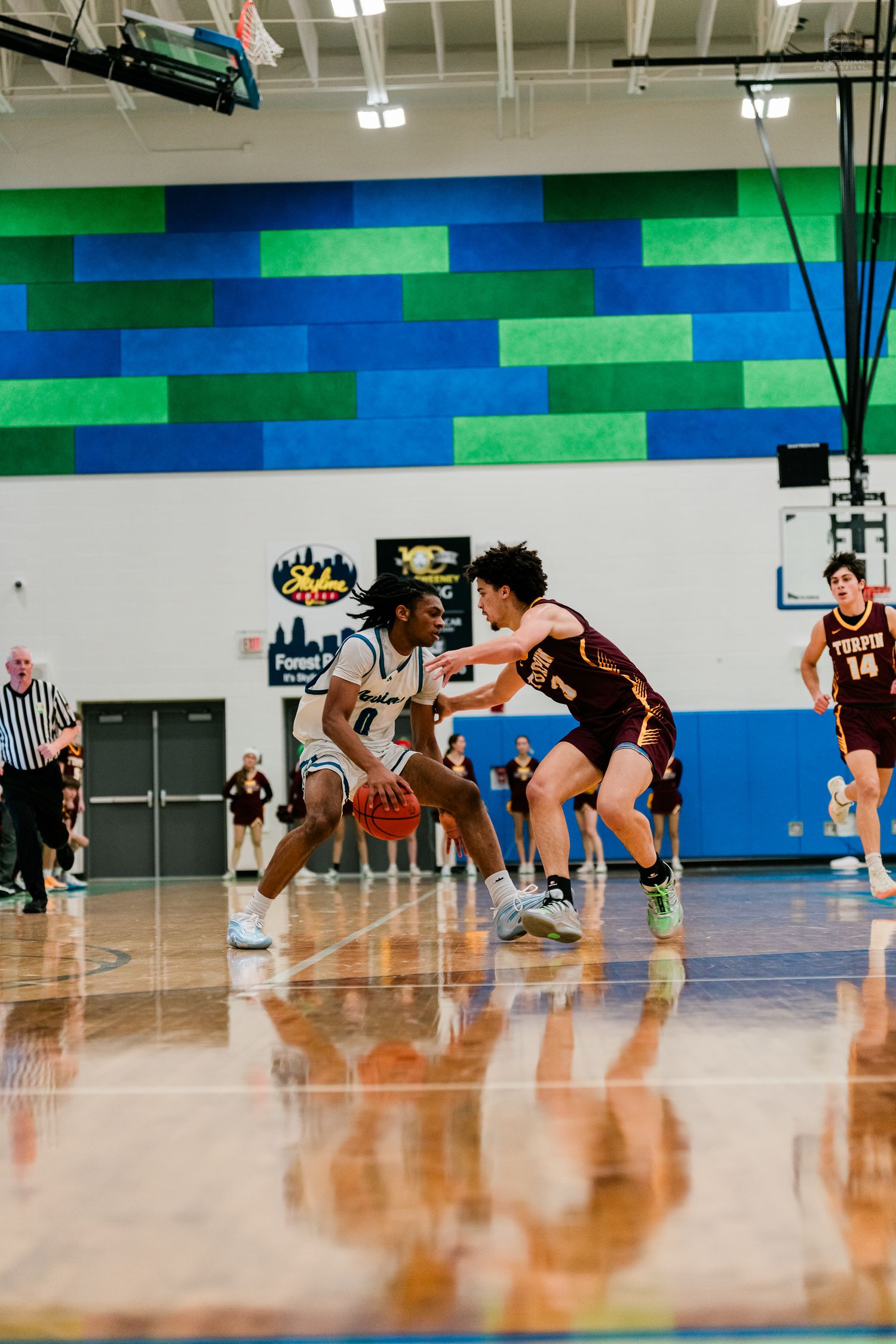A player in white dribbles while defended by a maroon-uniformed opponent during a high school basketball game.