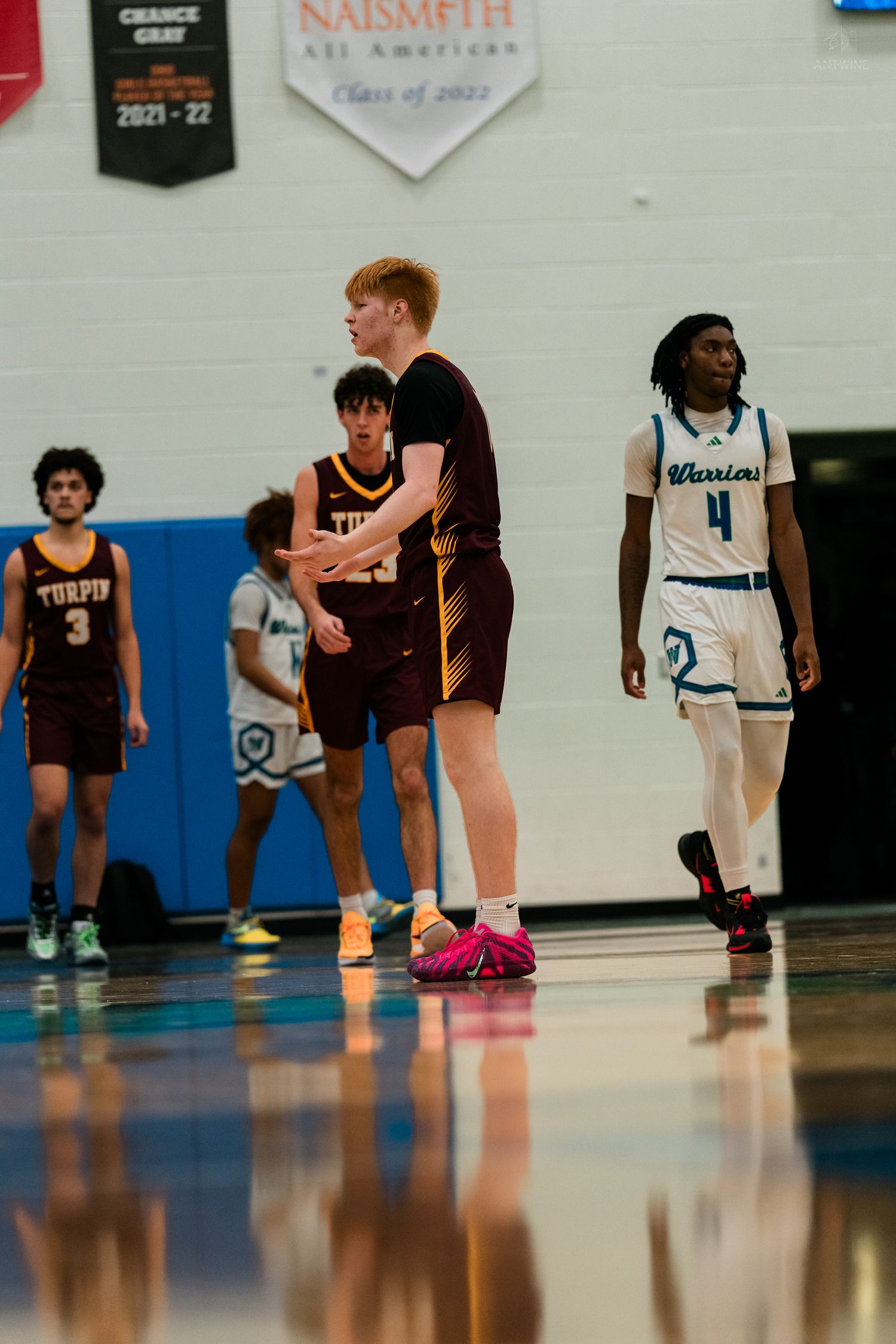 High school basketball players in maroon and teal Warriors uniforms during a game in a gymnasium.