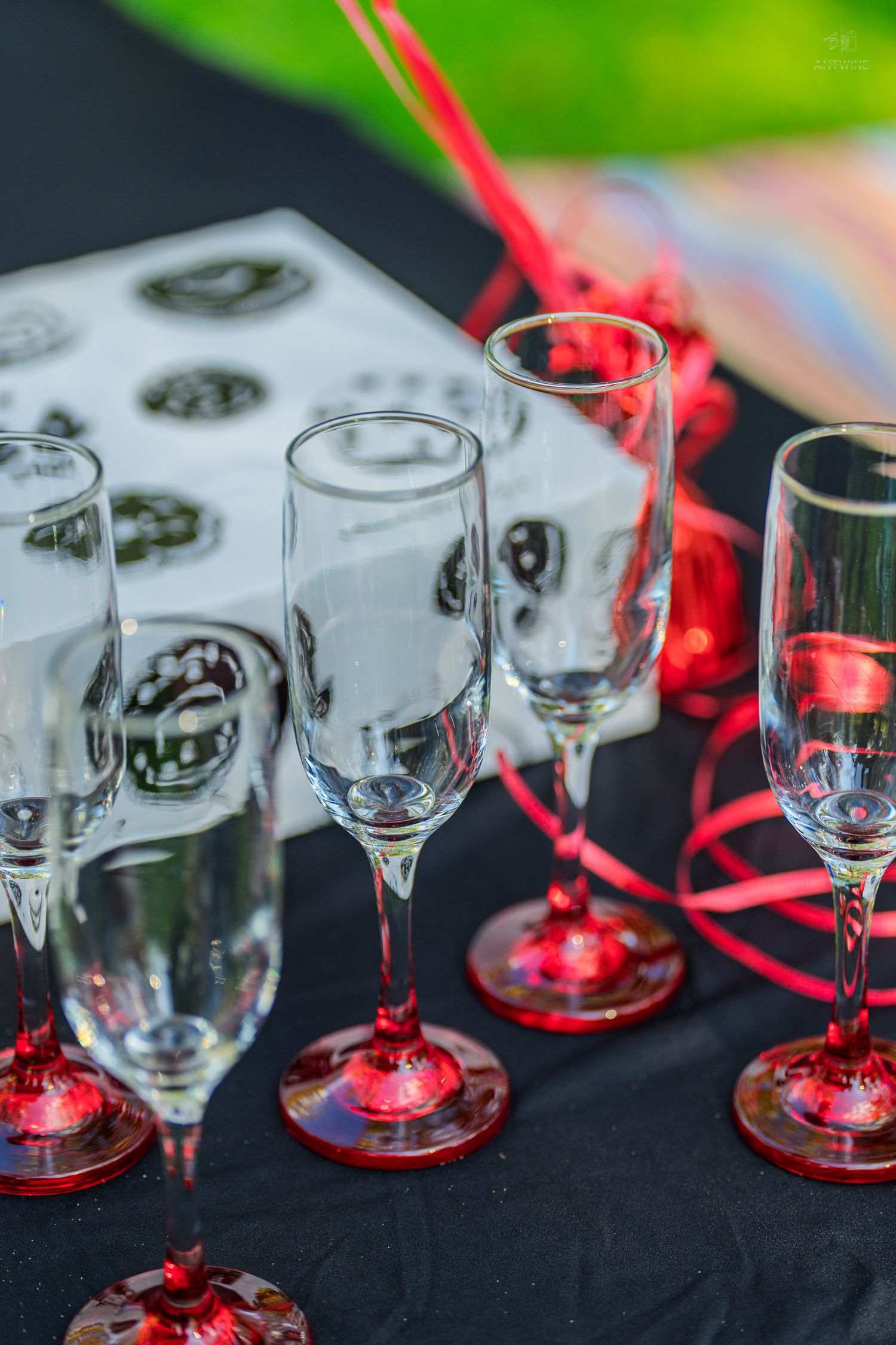 Empty champagne flutes with red bases and decorative red ribbons arranged on a black tablecloth for a celebration.