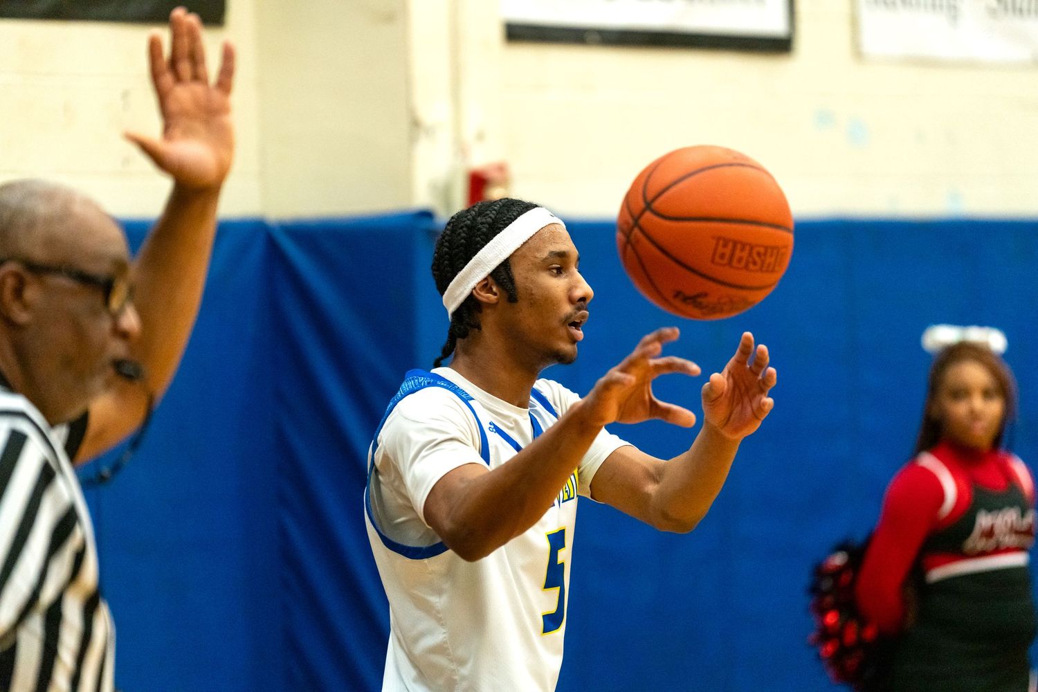 A basketball player in a white uniform catches a pass during a high school basketball game near the sideline.
