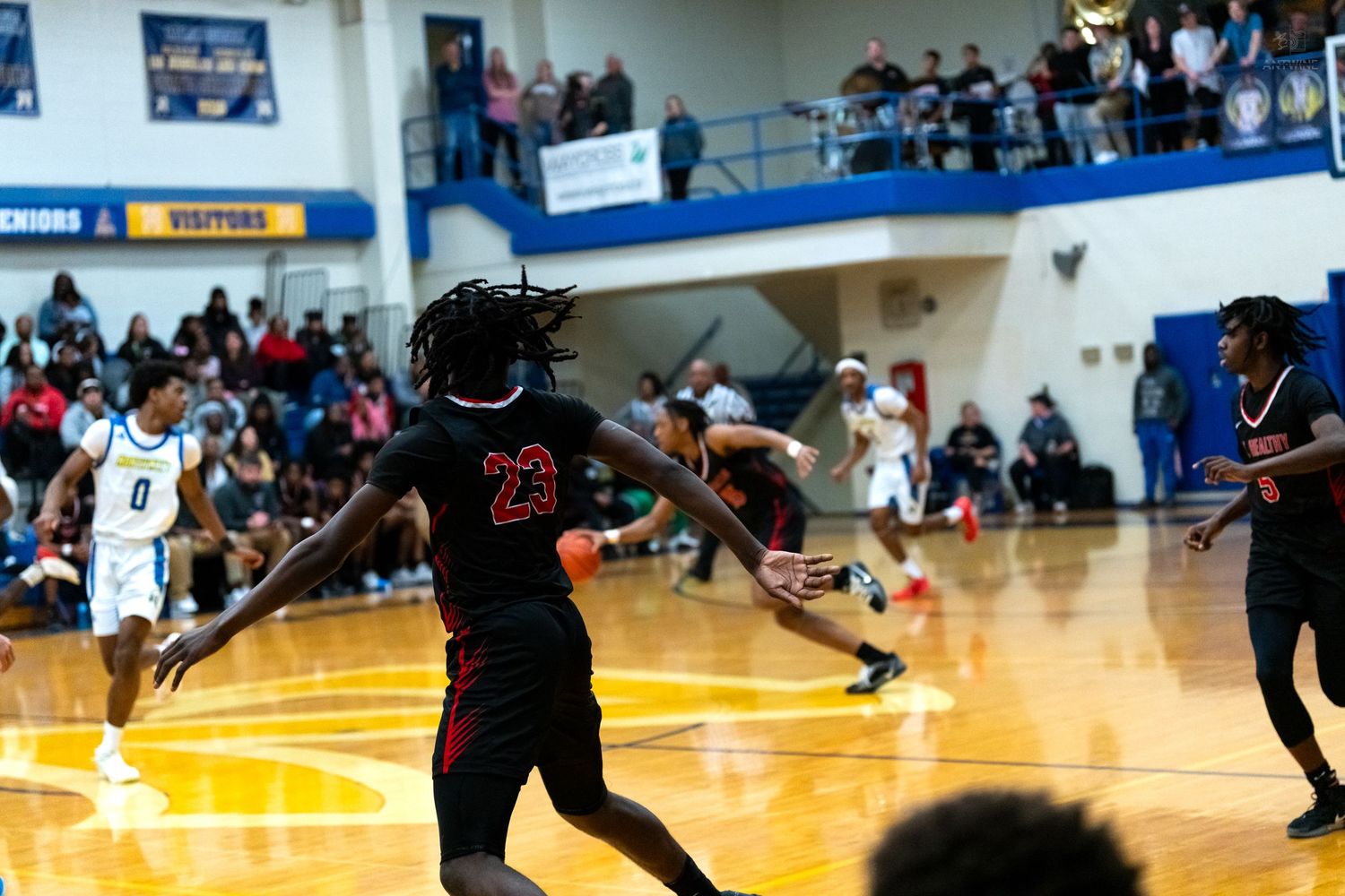 Player in red number 23 jersey dribbles during an intense high school basketball game with crowded bleachers.