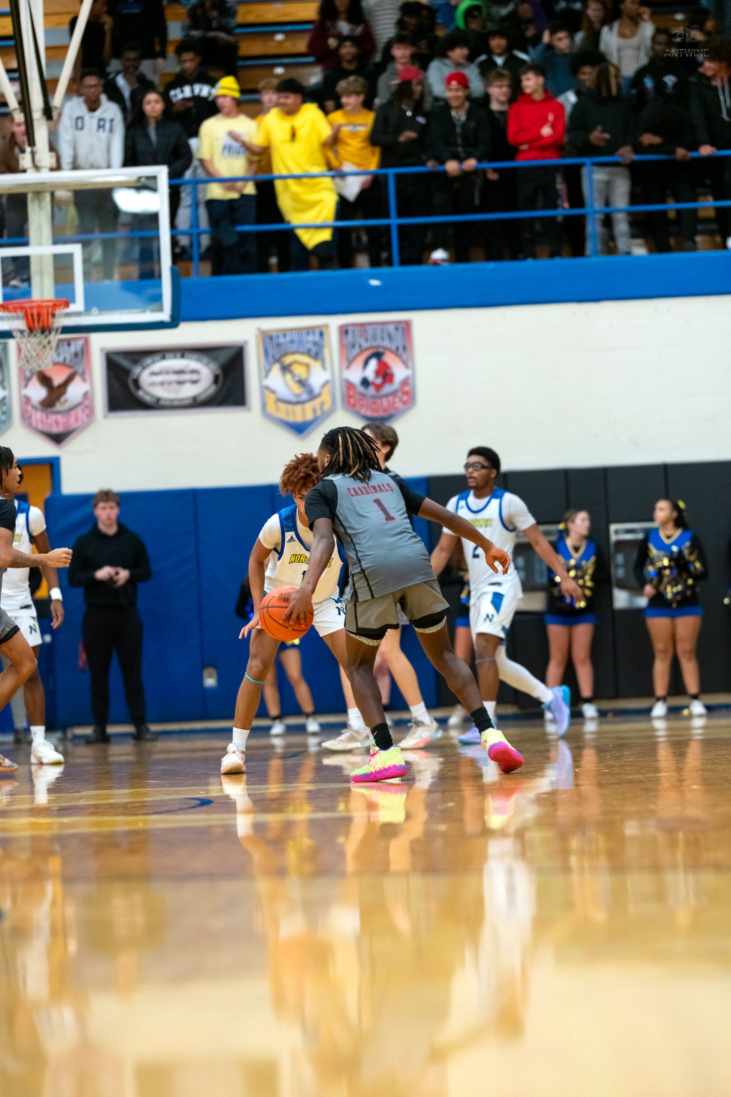 High school basketball players battle for position near basket in crowded gym.