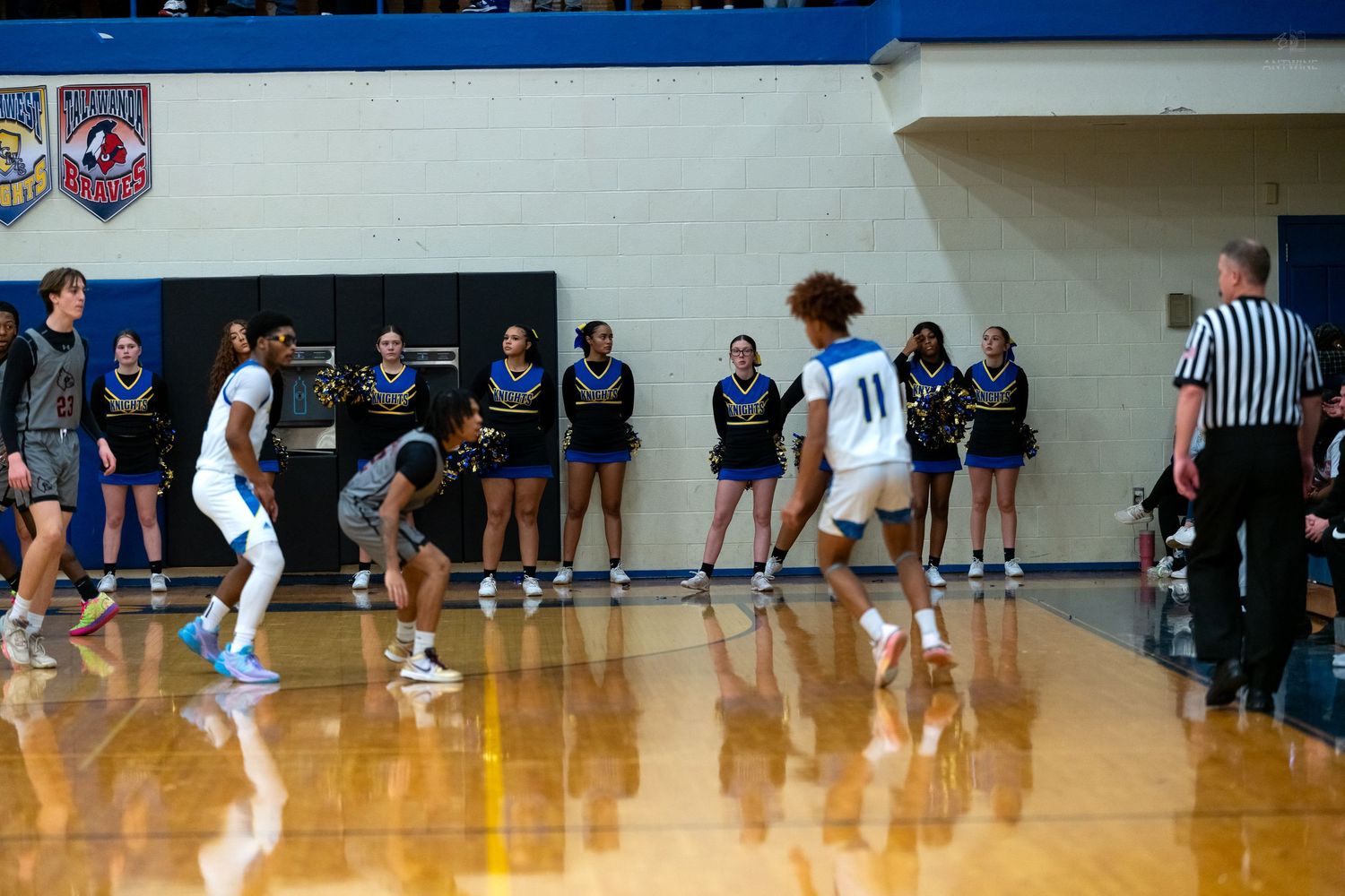 Basketball player number 11 dribbles near half court with cheerleaders and referee visible in background.