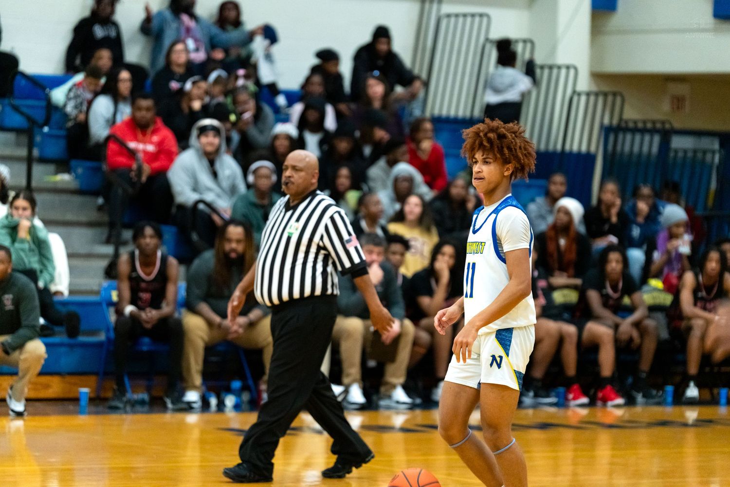 High school basketball player number 10 dribbles past a referee during a gymnasium game.
