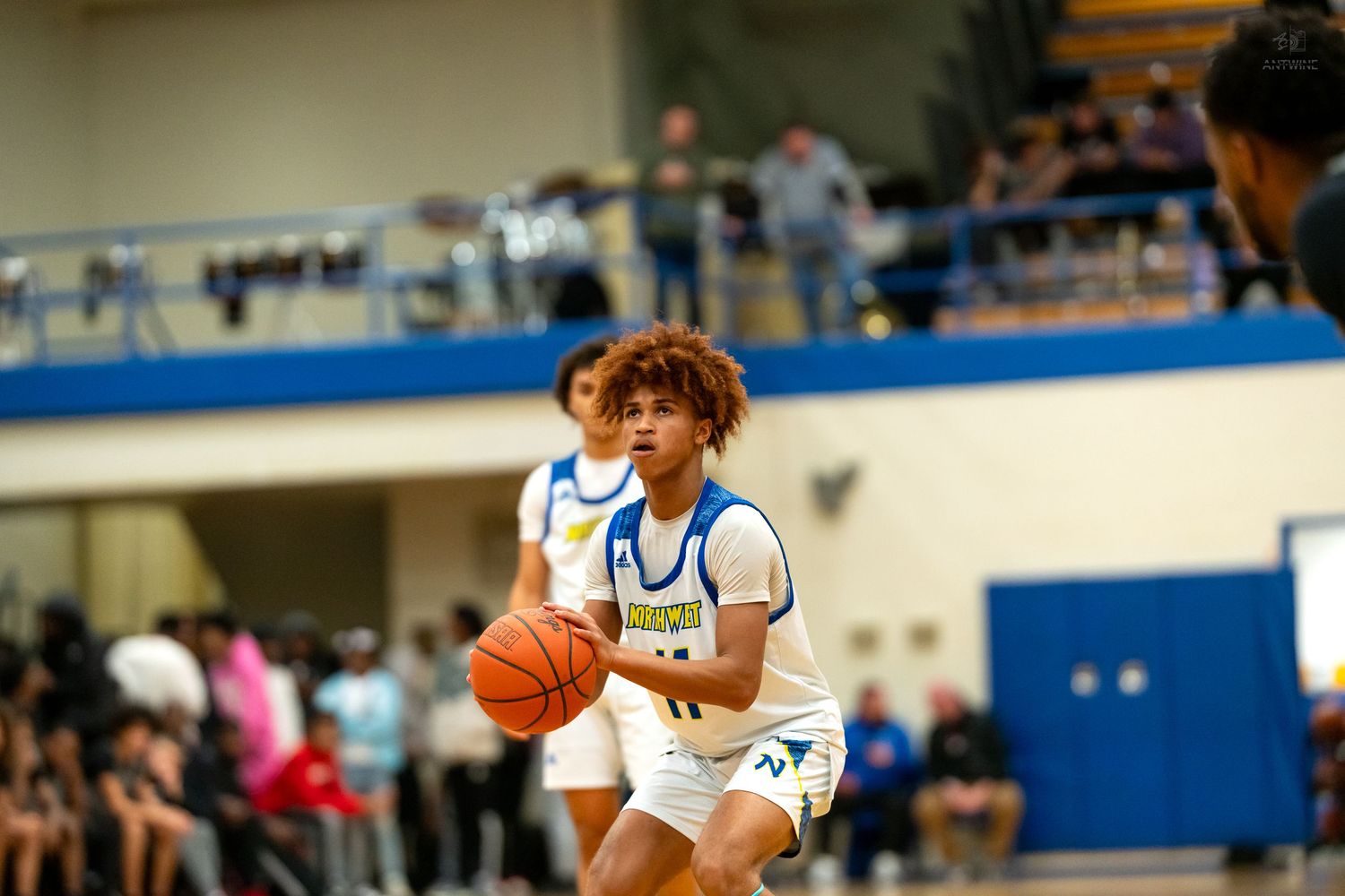 High school basketball player dribbles ball during game in blue and white uniform on indoor court.
