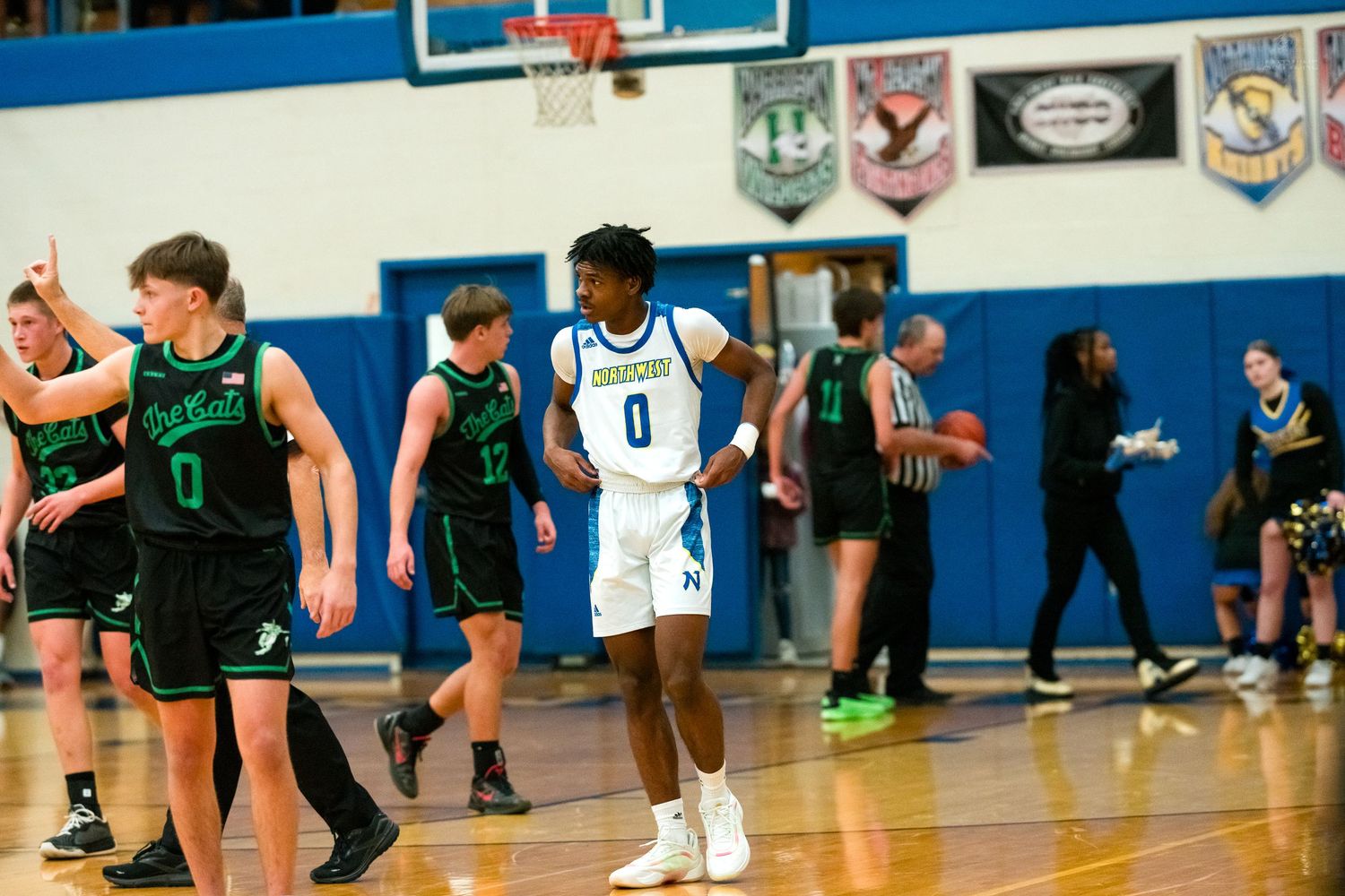 A blue-uniformed player wearing number 0 stands on court as green-jersey opponents walk nearby after a play.