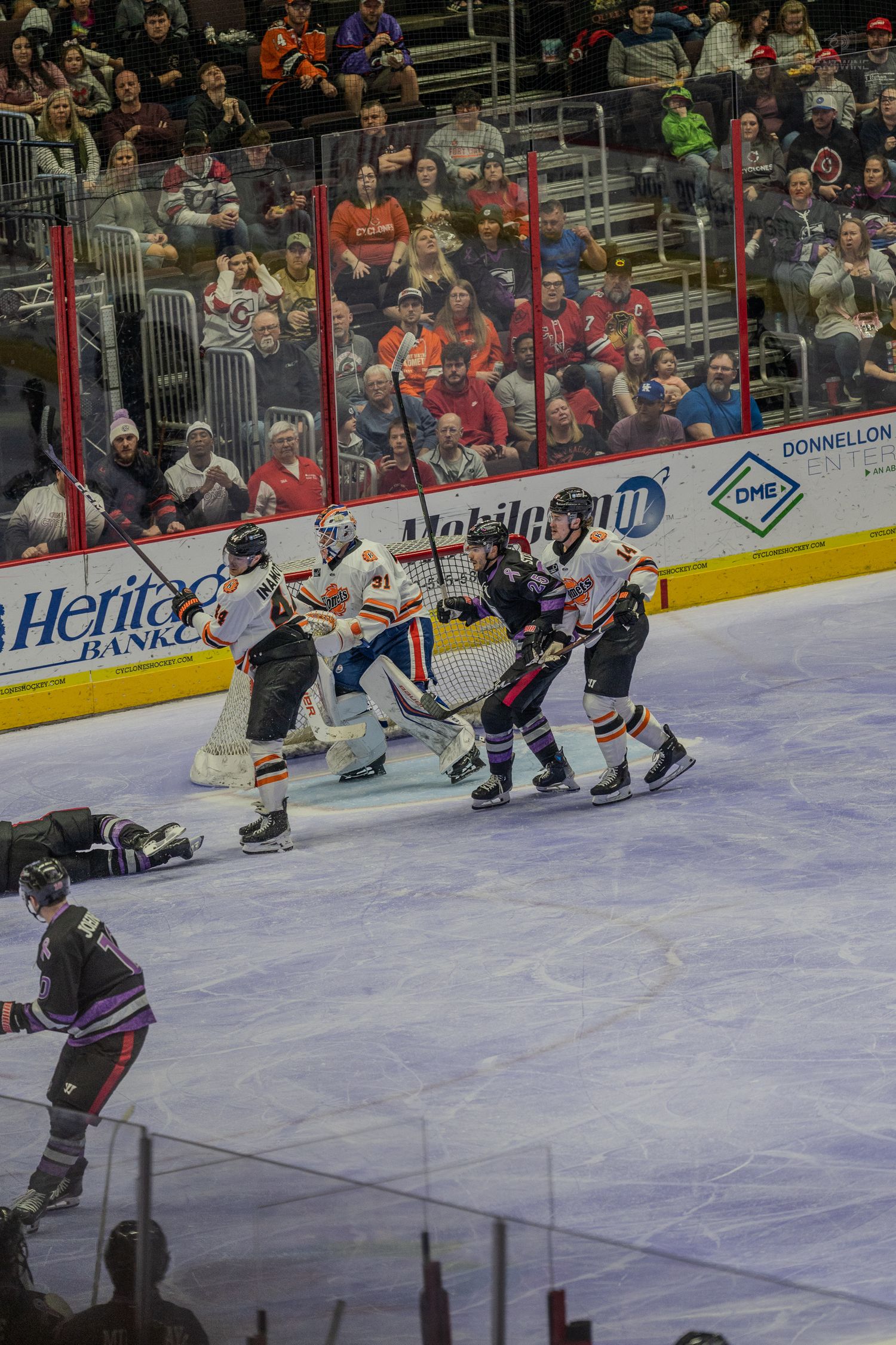 Ice hockey players battle near the goal crease as fans watch from the stands during an intense game.