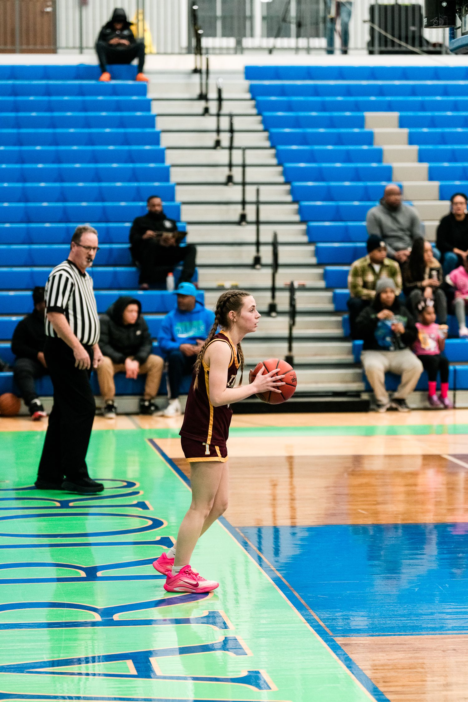 A female basketball player in maroon uniform prepares to inbound the ball near the sideline.