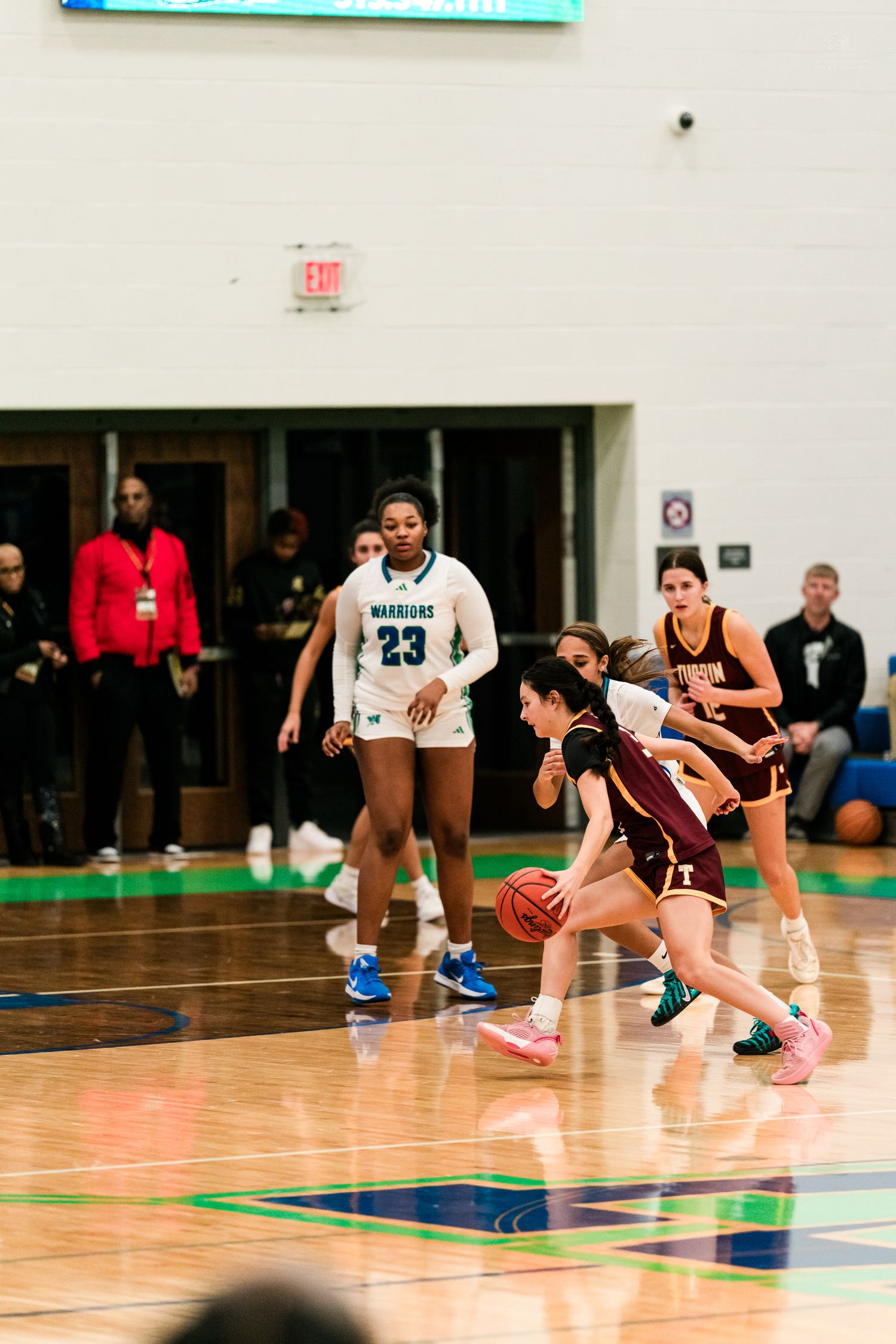 Turpin girls basketball player dribbles past Warriors defender number 23 during high school game.
