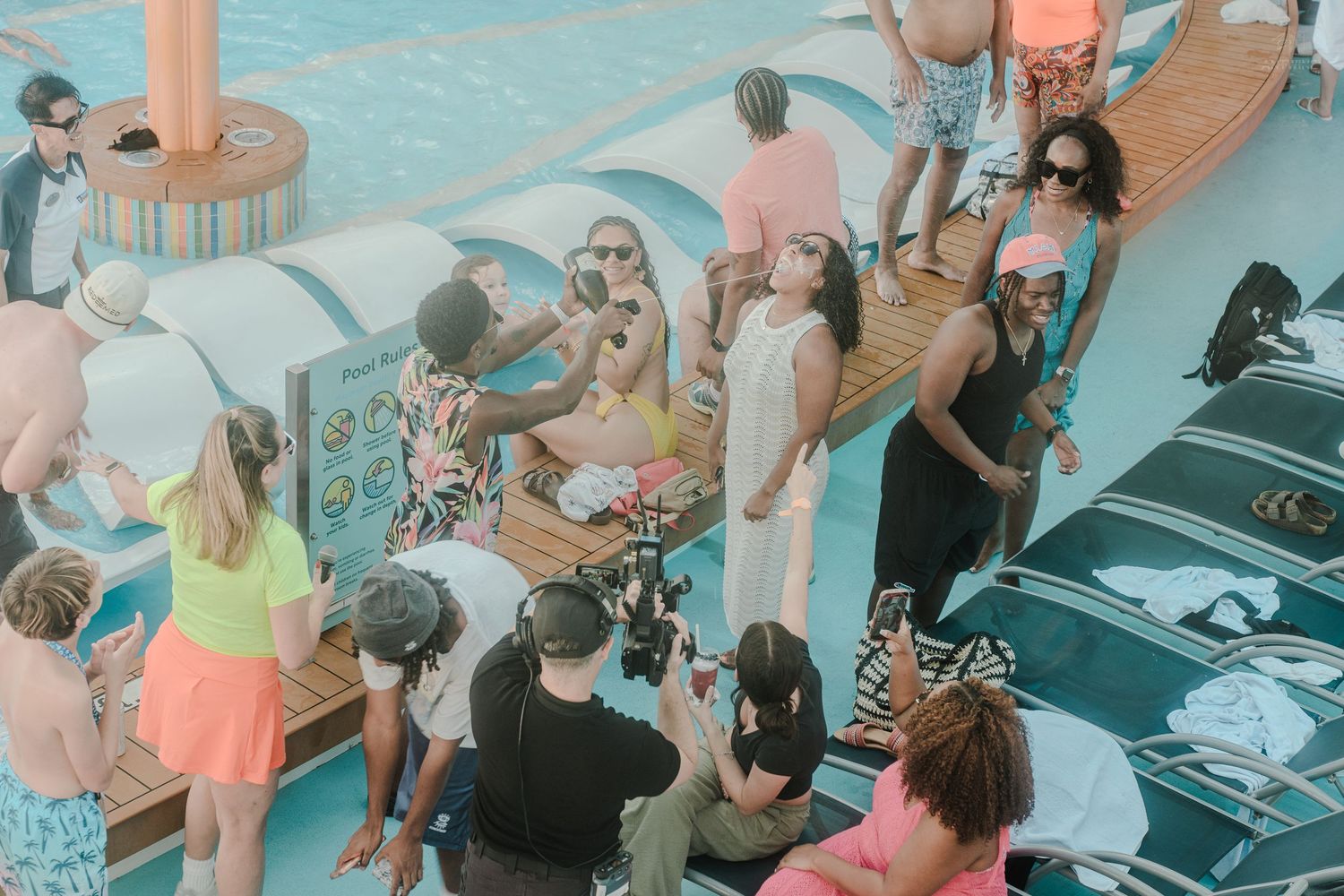 Cruise passengers gathering and taking photos together near a pool on a sunny ship deck.