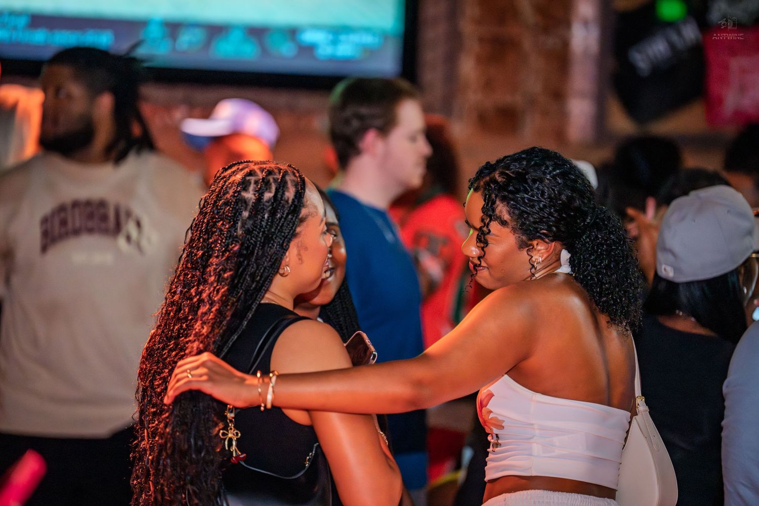 Two women with curly hair embracing and dancing together in a lively nightclub.