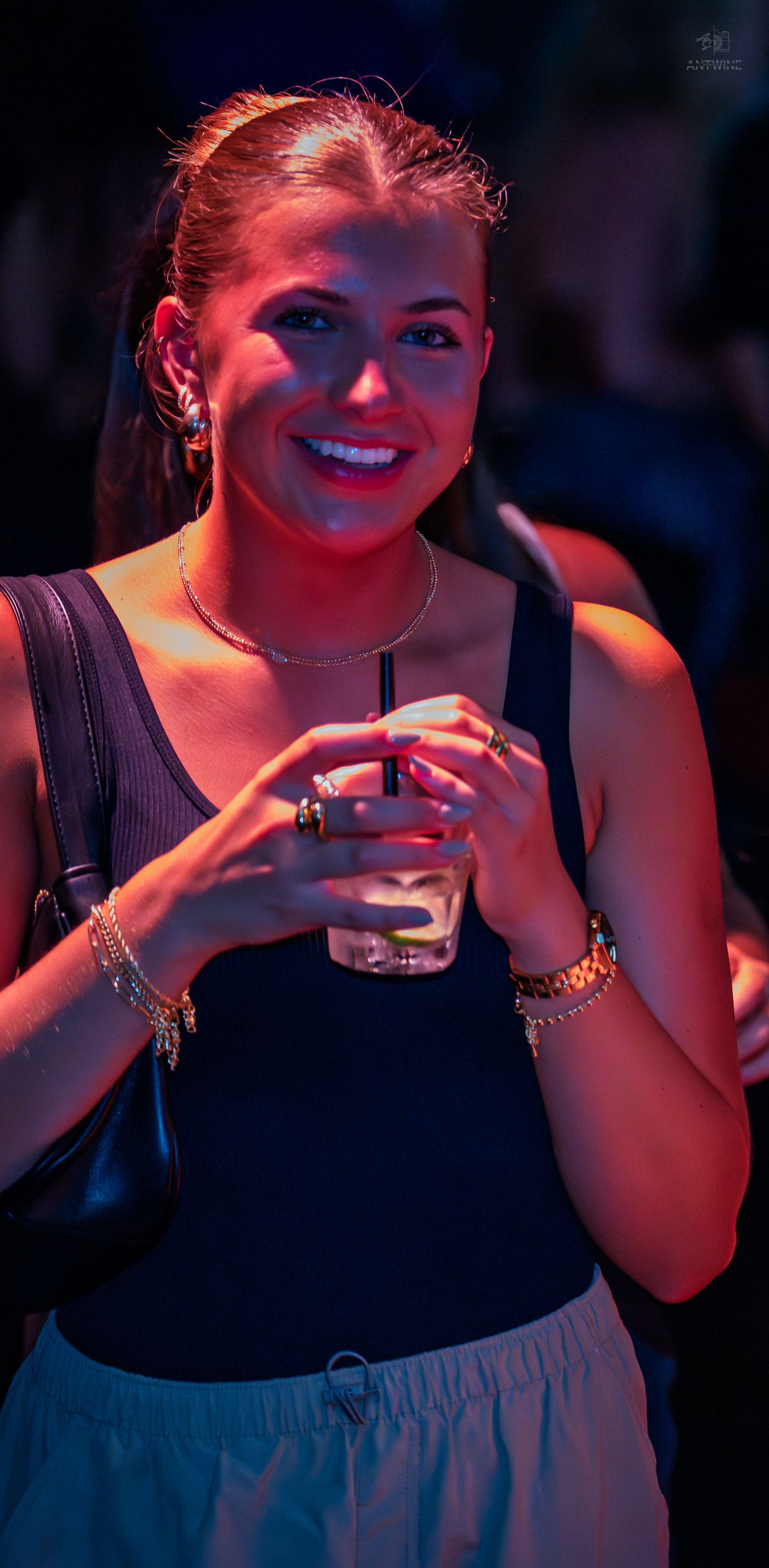 Smiling woman holding drink at colorful nightclub event with neon lighting.