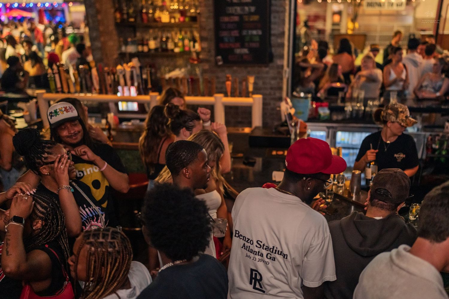 Energetic crowd gathered around a busy bar with colorful lighting at a nightclub event.
