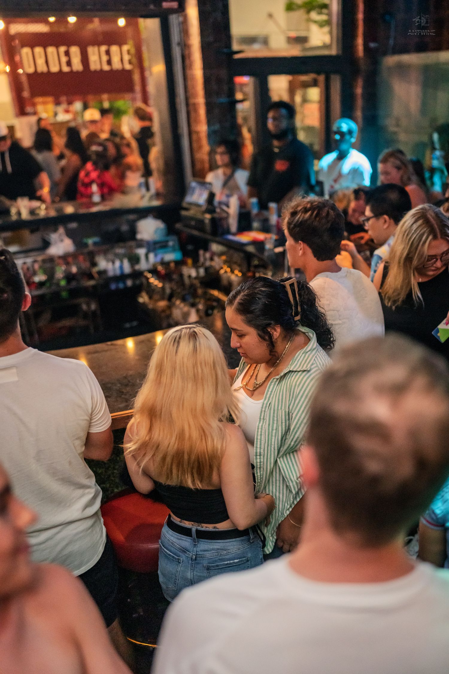 Bar patrons mingling near an Order Here sign at a busy nightclub.