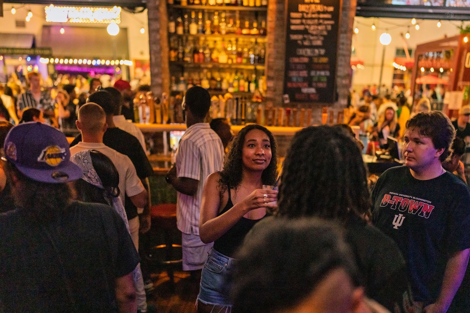 Diverse crowd socializing near a fully stocked bar with warm ambient lighting.