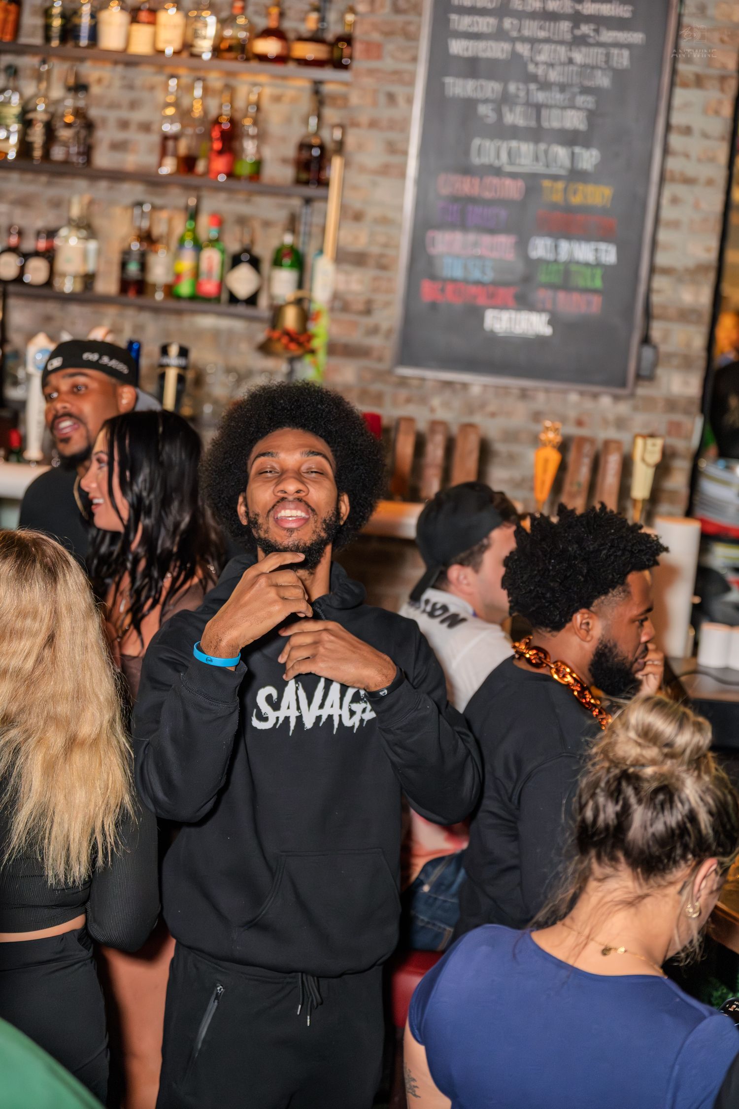 Man in Savage hoodie smiling at the camera near a bar.