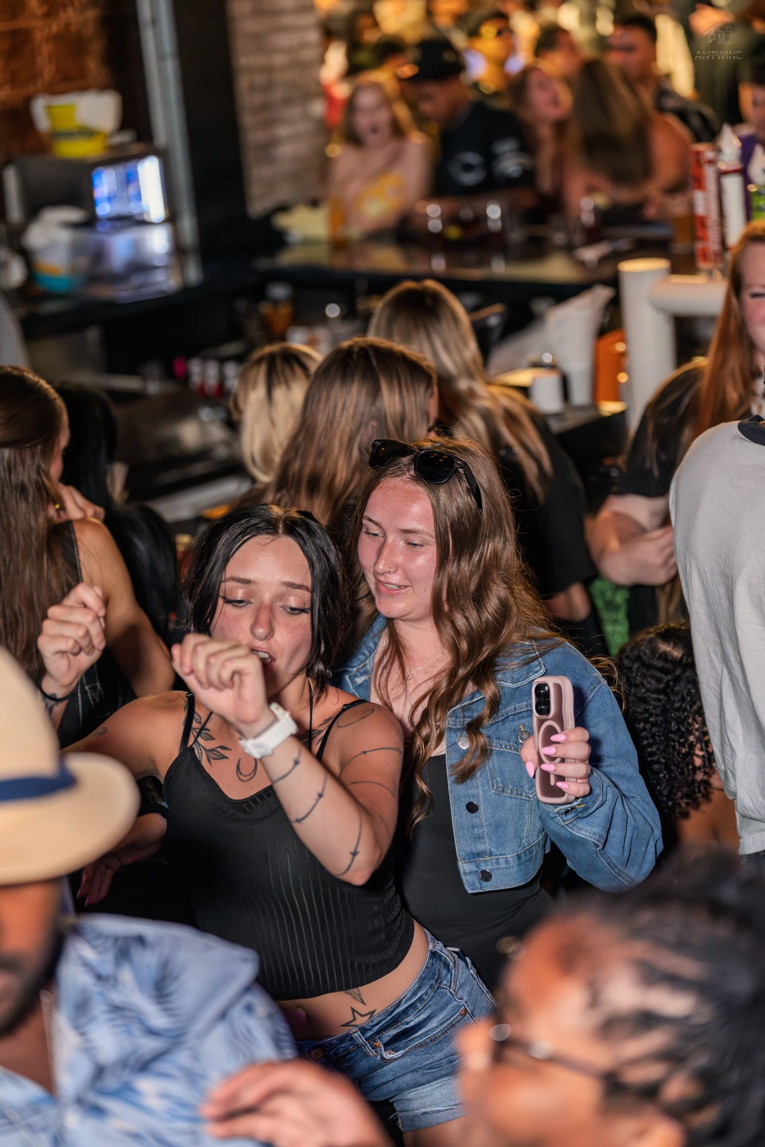 Two young women dancing together at a lively bar, one holding a drink and smiling.