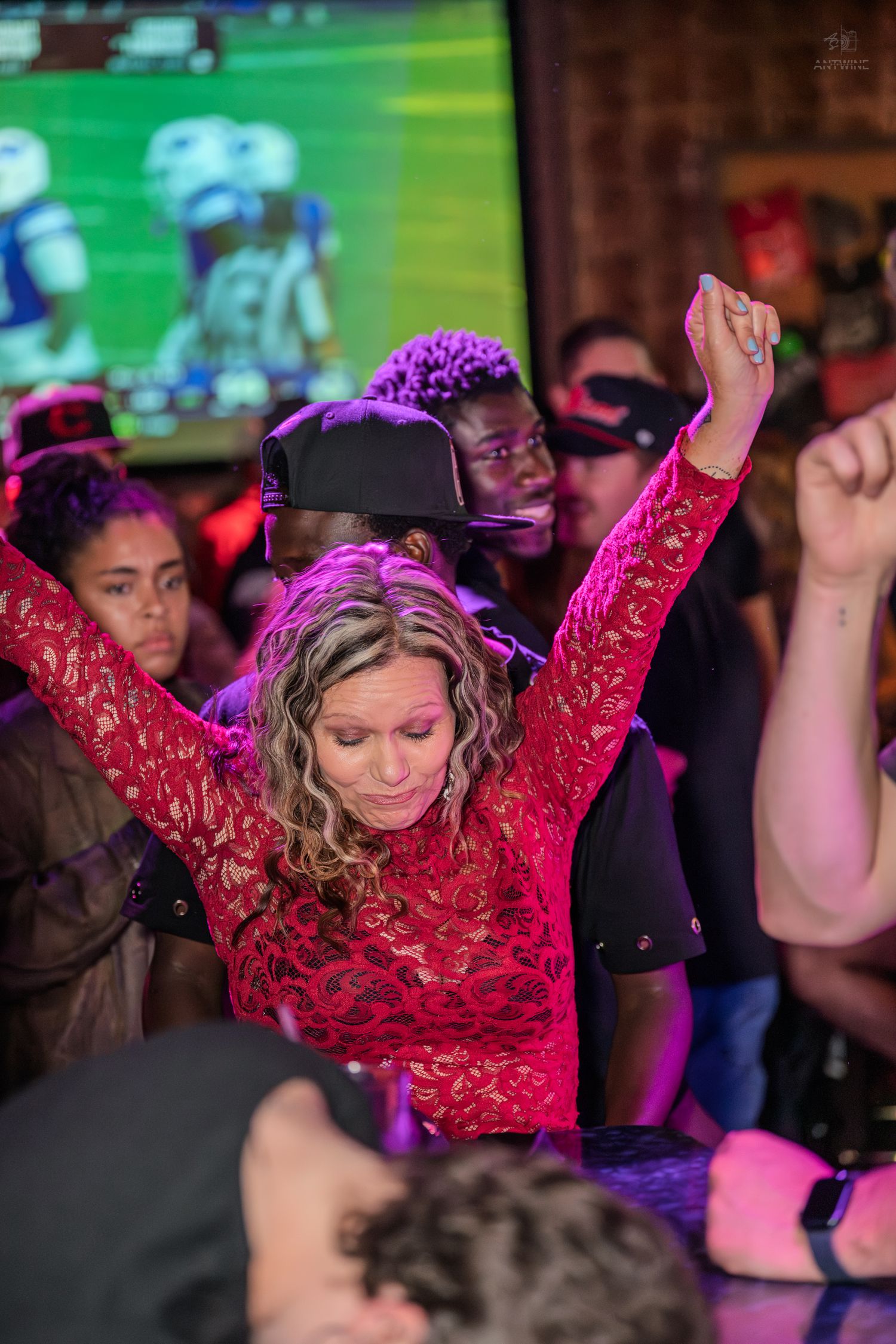Woman in red lace dress dancing with arms raised under pink lights at a packed nightclub.