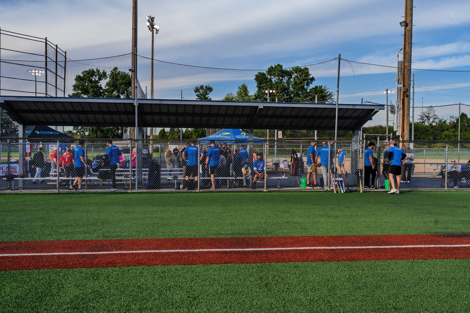 Baseball team in blue uniforms gathered near dugout on artificial turf field at dusk.
