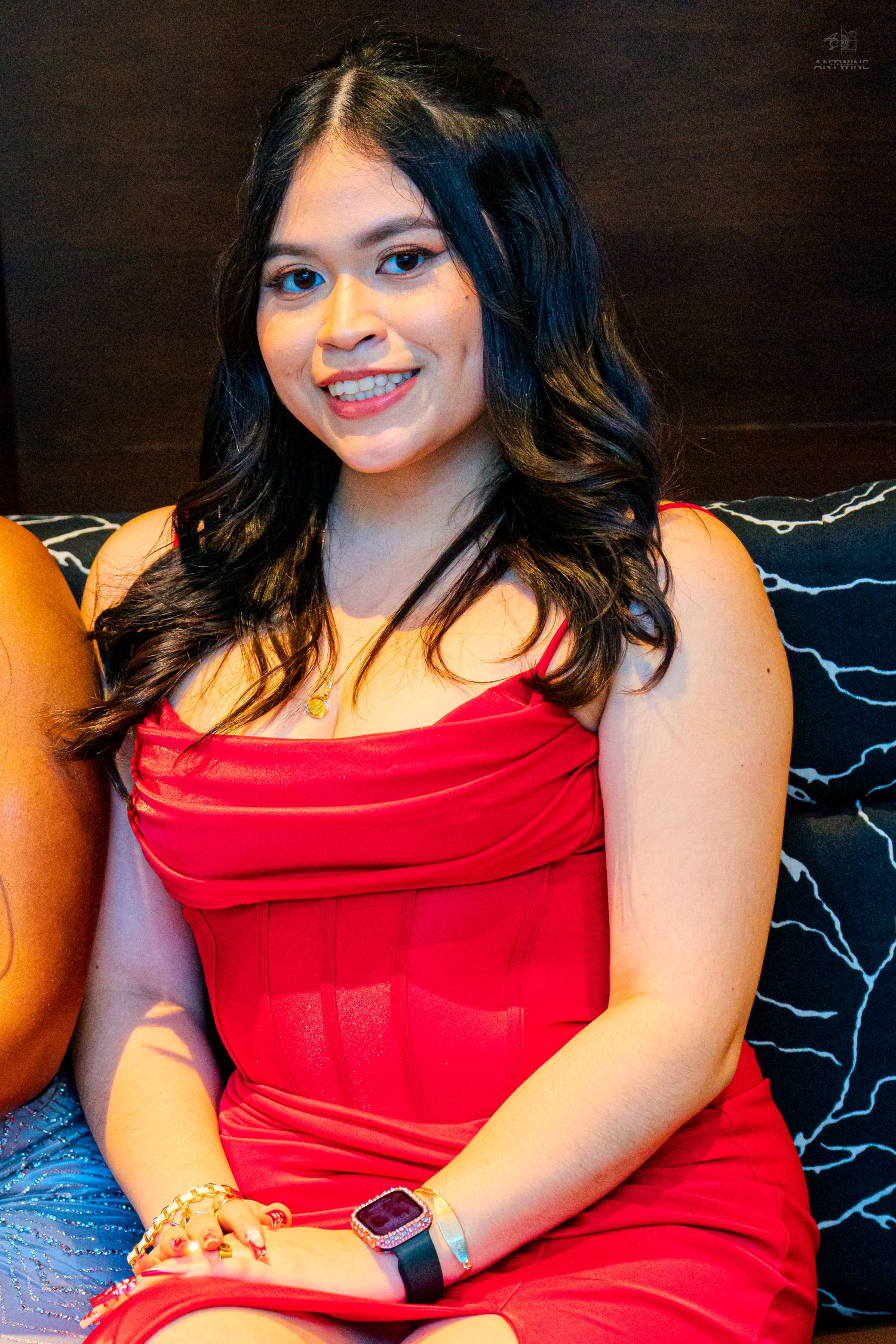 Young woman in a red dress smiling, wearing braces and a smartwatch, seated on a couch.