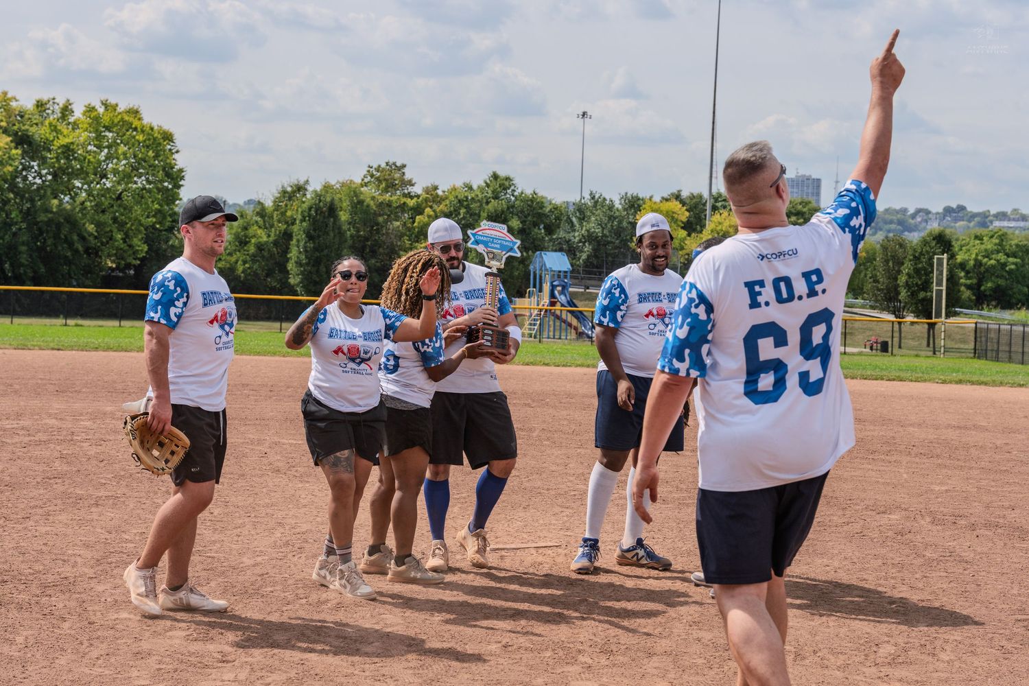 Charity softball game players celebrate on the field wearing matching blue and white team uniforms.