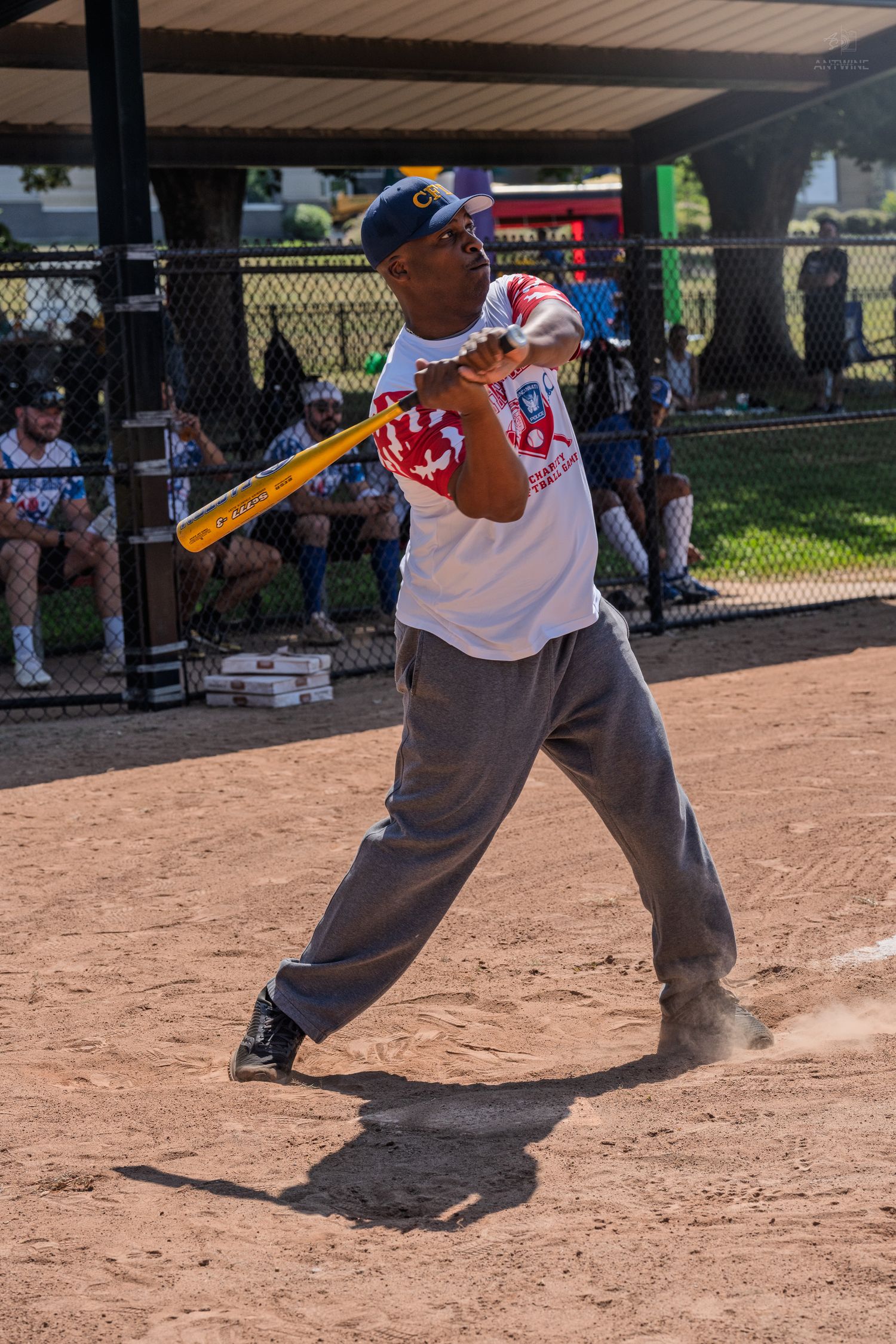 A softball batter follows through on a powerful swing during an outdoor baseball game on a sunny day.