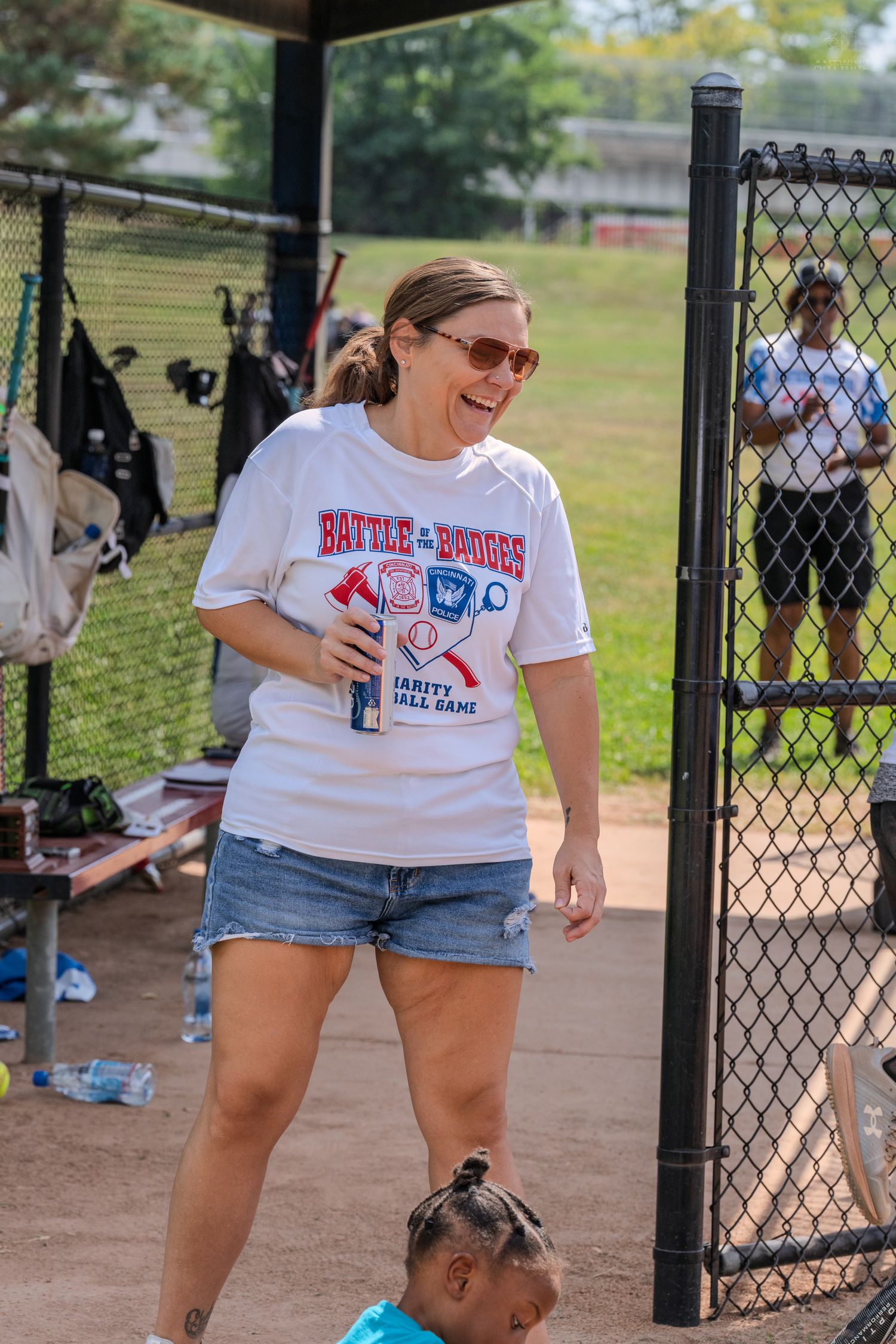 Woman in a Battle of Badges charity softball game t-shirt and denim shorts laughing on the field.