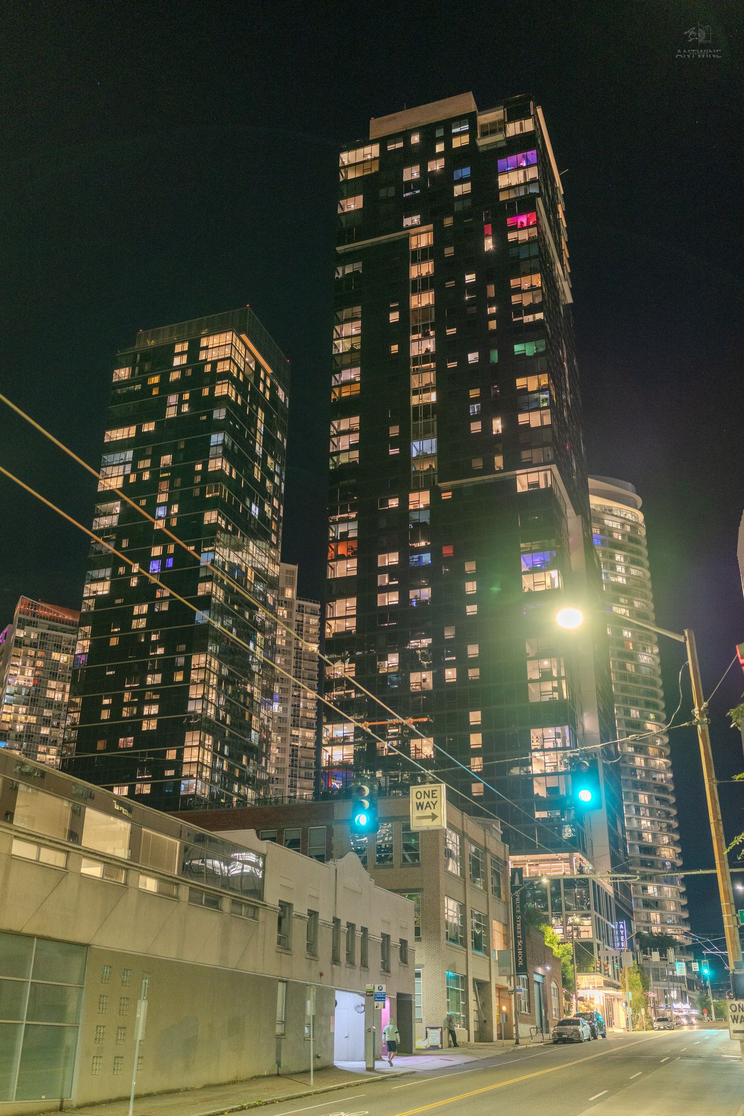 Night cityscape of tall illuminated skyscrapers along an empty urban street with glowing traffic lights.