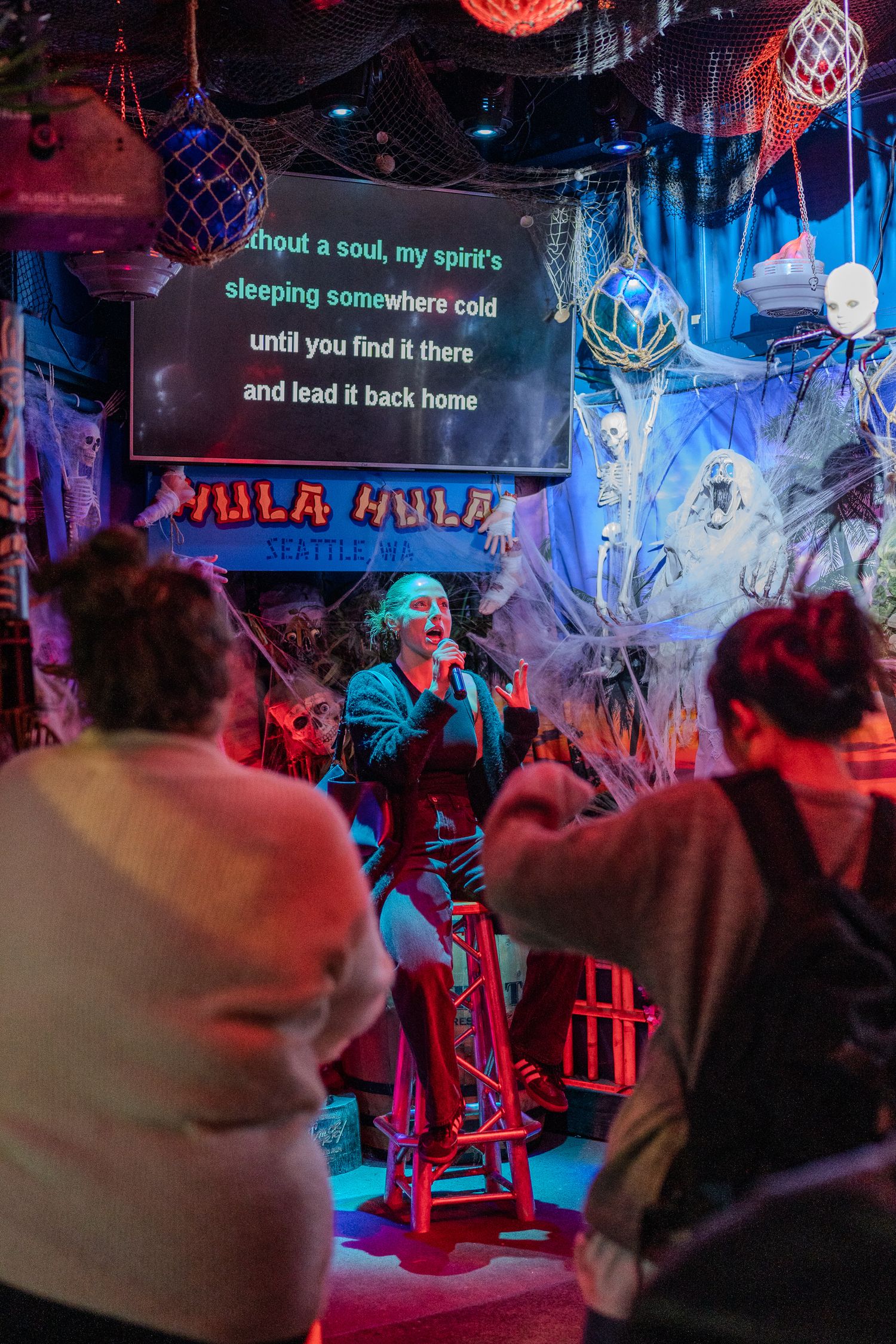 Woman performing karaoke at spooky Halloween-themed Hula Hula bar Seattle with audience watching.