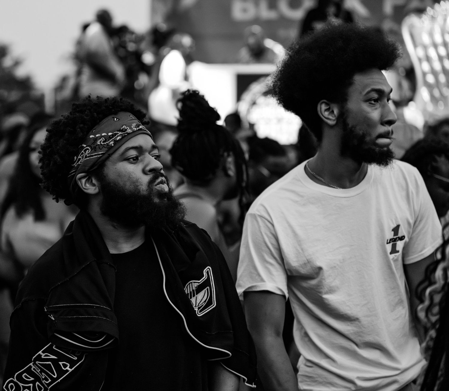 Two Black men with natural hair and beards stand together at an outdoor gathering in a black and white photo.