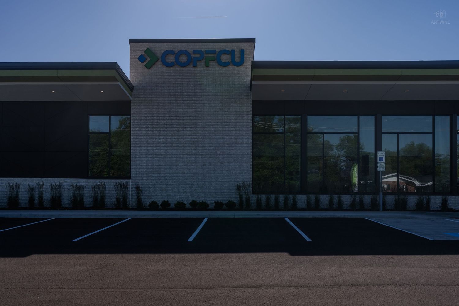 COPFCU credit union modern building exterior with illuminated signage, stone facade, and empty parking lot at dusk.