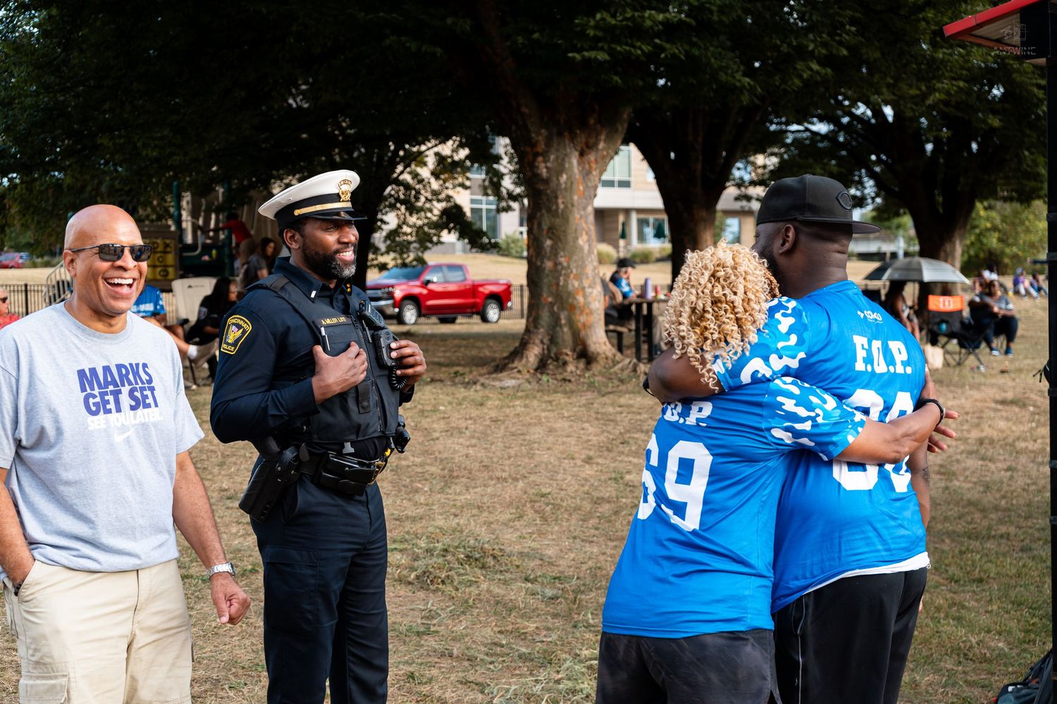 A police officer laughs with community members wearing FOP jerseys at an outdoor event on a sunny day.