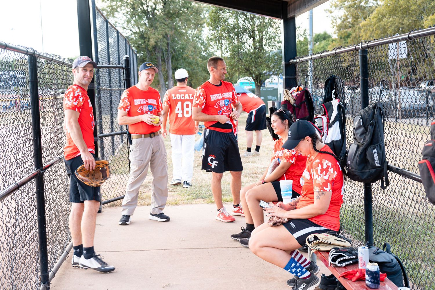 Softball team in red uniforms resting in dugout during game.