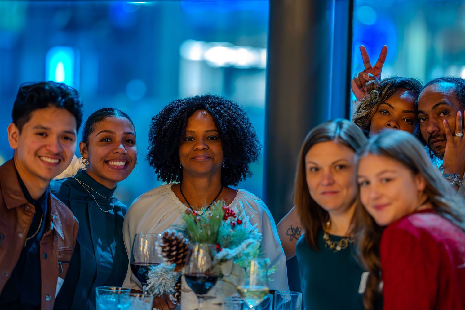 A diverse group of smiling friends posing together at a festive indoor gathering with holiday decorations.