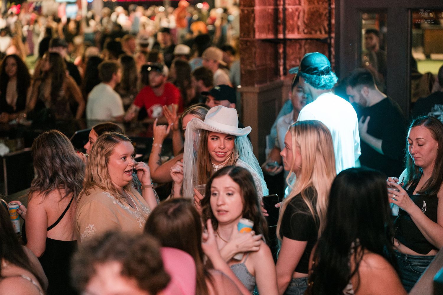 Large group of women socializing at a busy nightclub, one in a white cowboy hat.