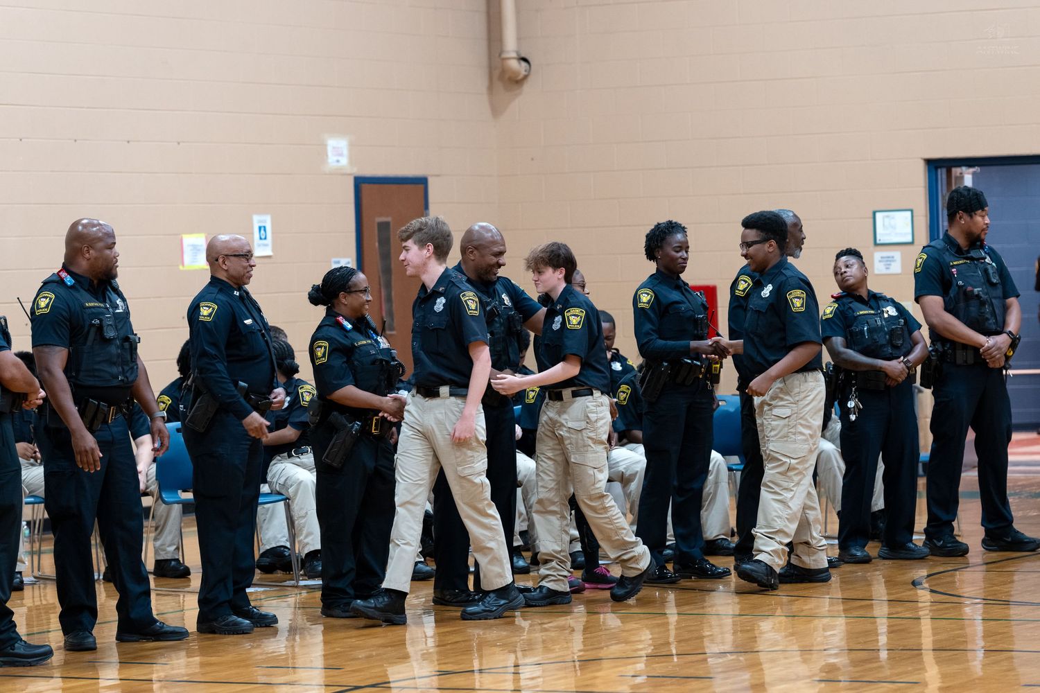 Police officers in black uniforms gathered in a gymnasium during an official recognition ceremony.