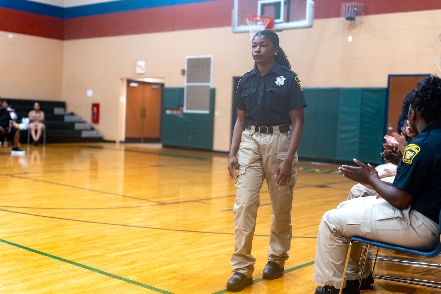 Young student in uniform speaks confidently in school gymnasium during a presentation or drill exercise.
