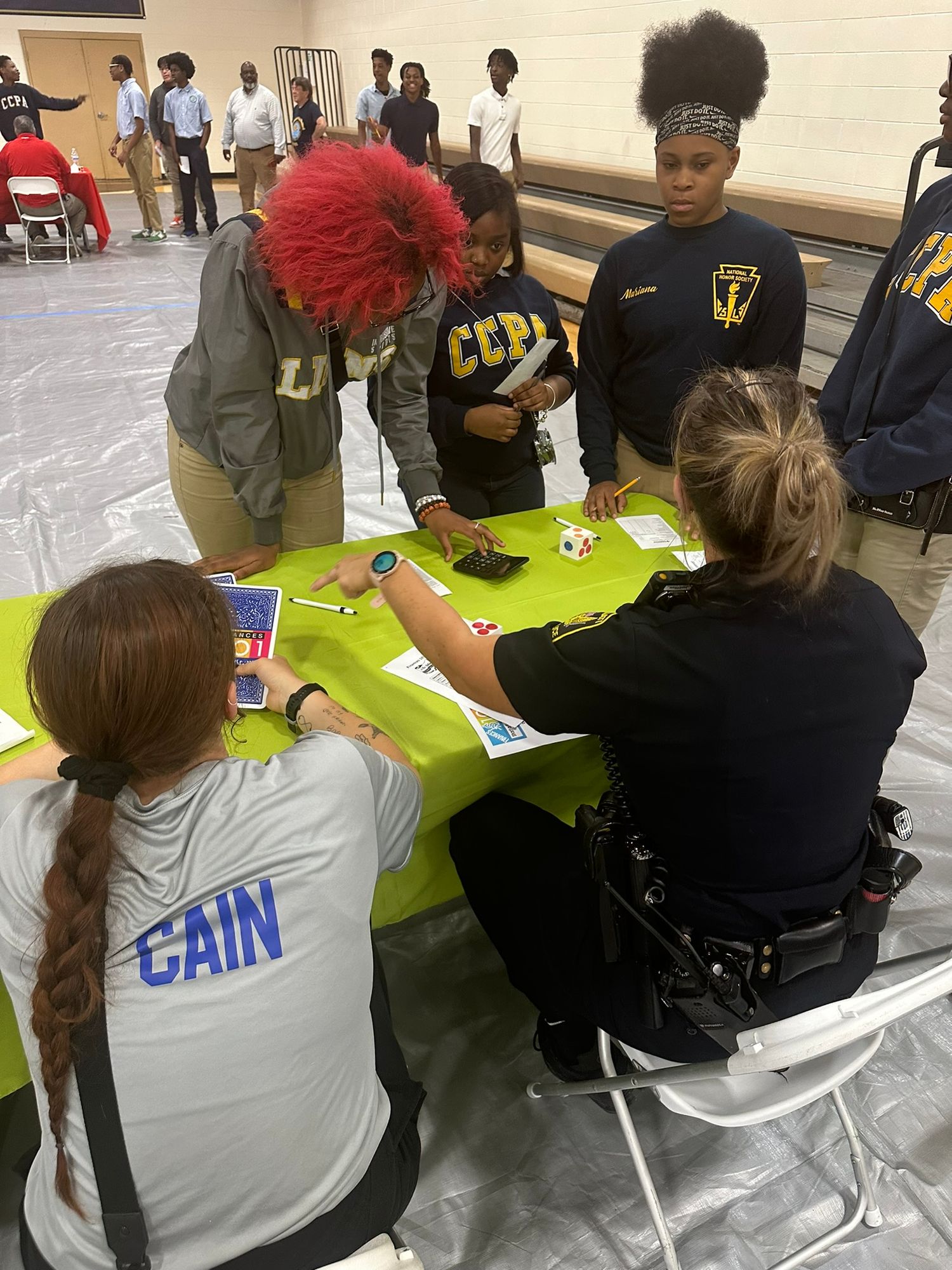 Officer Cain and colleagues engage students in an educational activity at a school event with a green table.