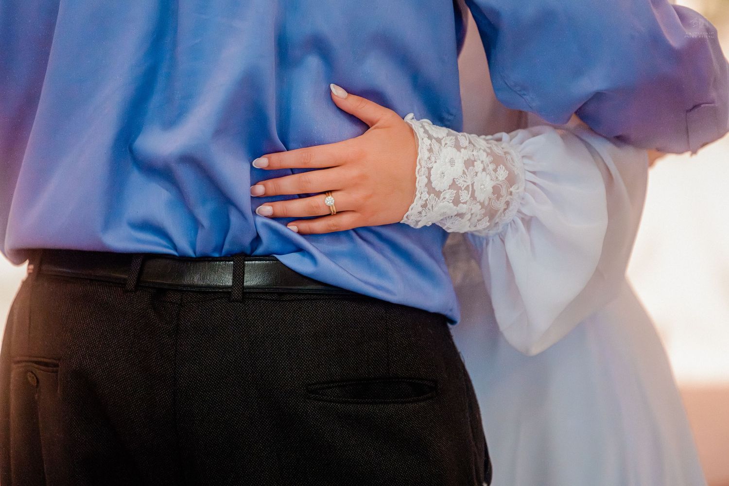 Bride in lace sleeve wedding dress places hand on grooms back during romantic first dance.