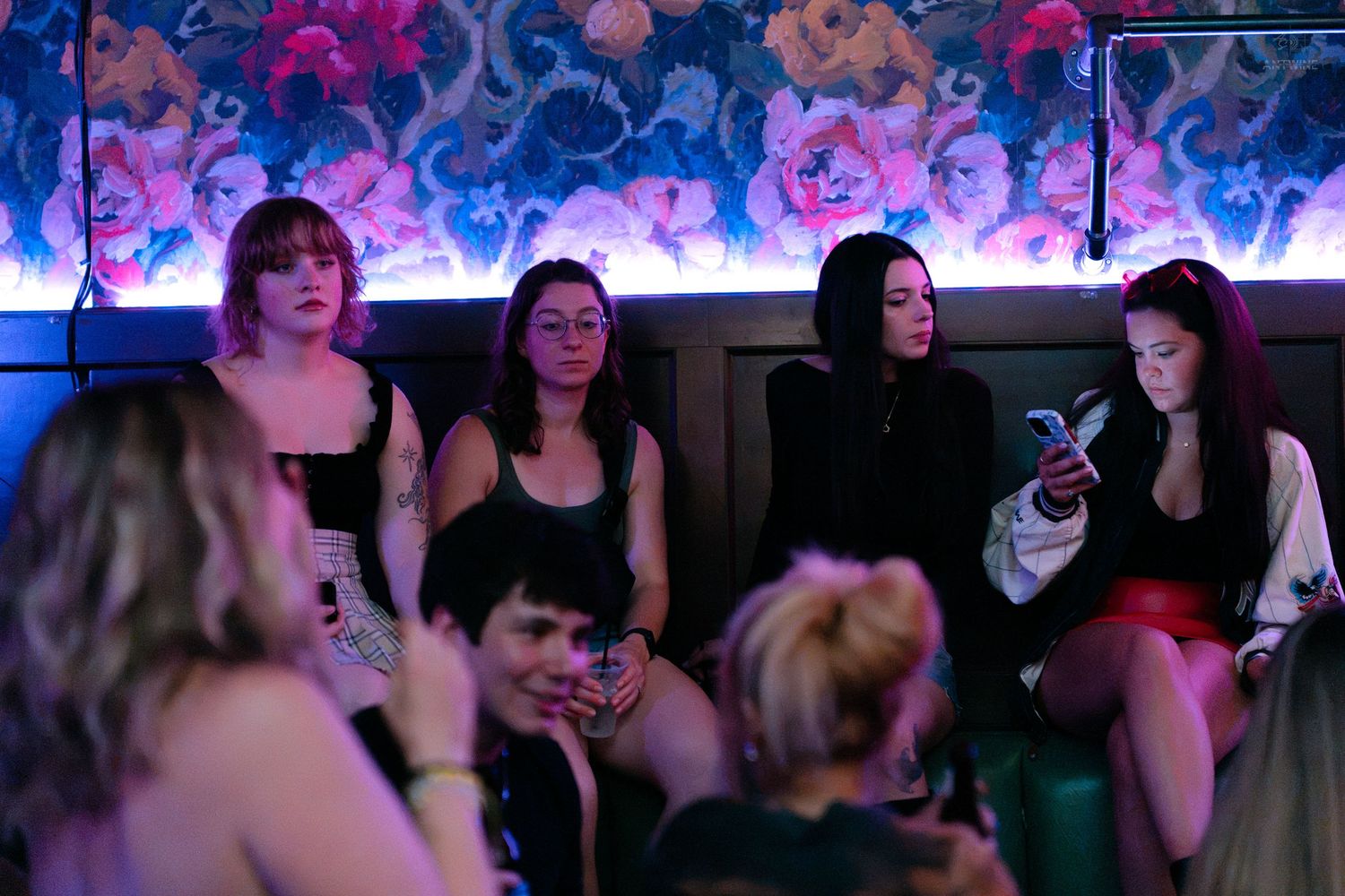 Group of young women relaxing on a couch in a neon-lit nightclub lounge.
