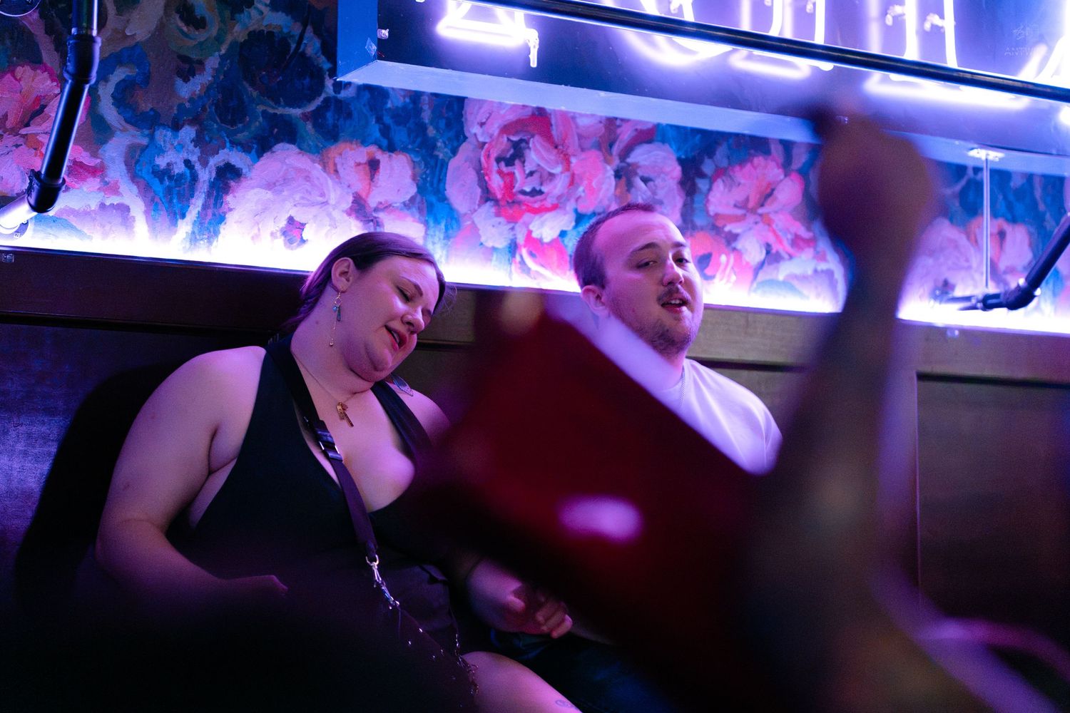 Two people laughing and enjoying themselves at a nightclub with neon lights and floral decor.