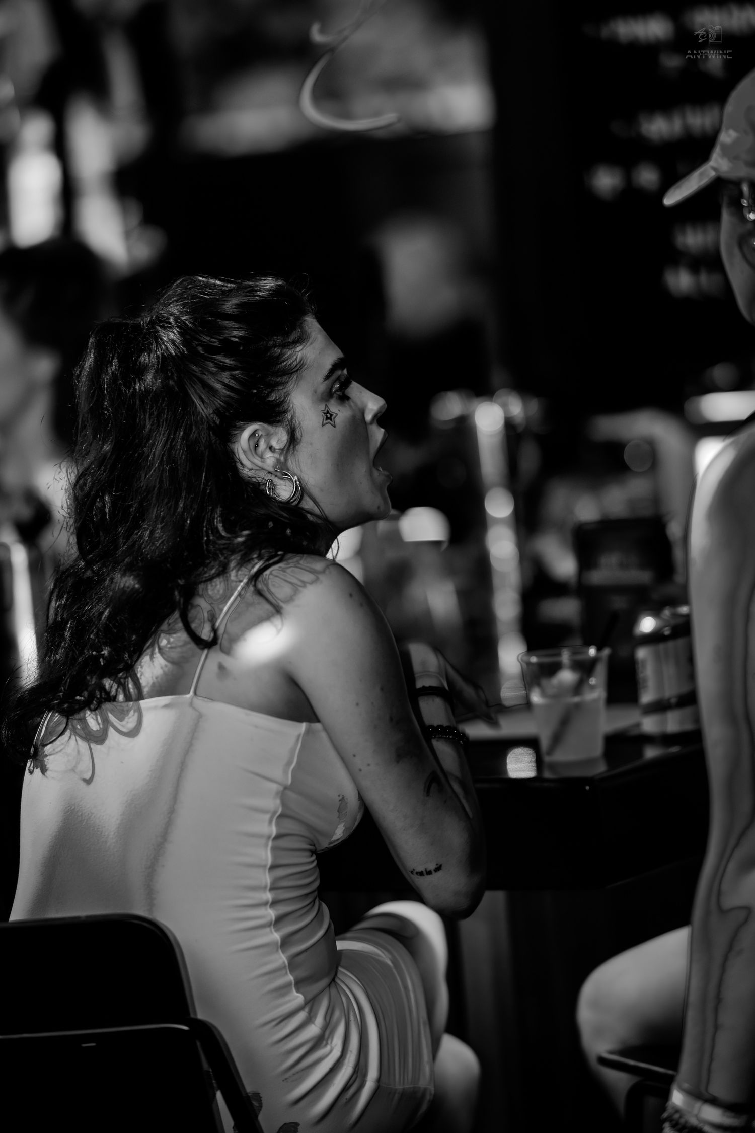 Black and white photo of a woman in a slip dress sitting pensively at a bar counter.