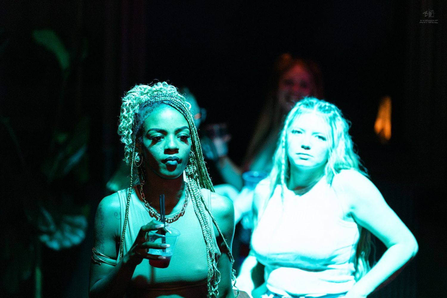 Two women illuminated by teal light at a nightclub event or performance.