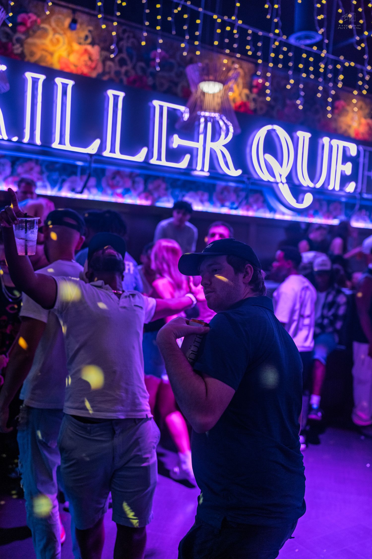 Guests dancing beneath a bright Killer Queen neon sign in a vibrant club.