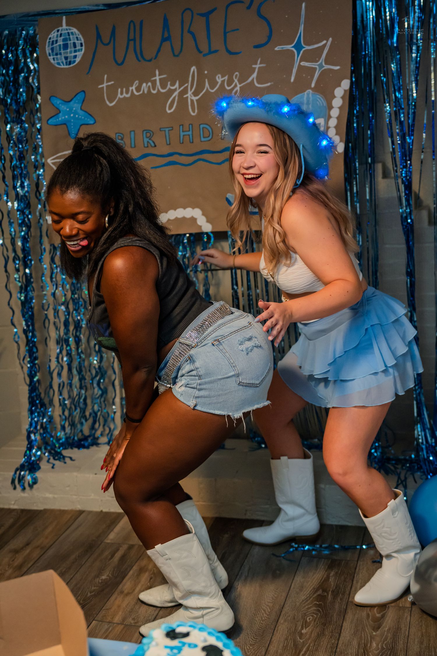 Two friends dance and laugh together at Malarie's 21st birthday party with blue streamers.