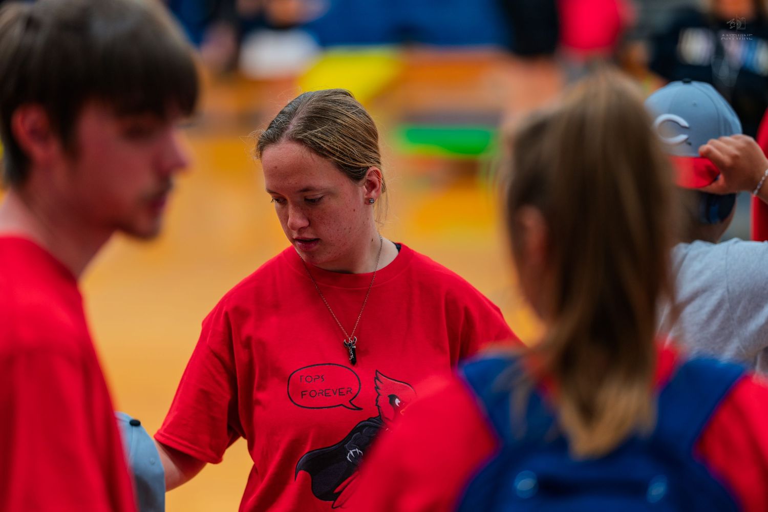 Young athletes in red team shirts gather on a gymnasium floor during a sports event or competition.
