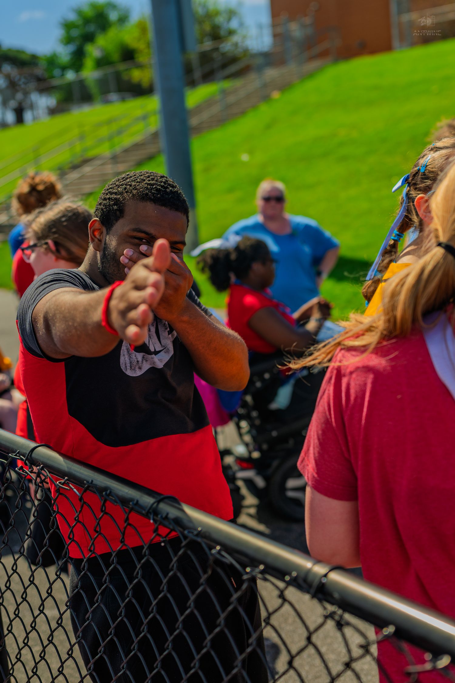 A man in a red shirt reaches over a chain-link fence to greet someone at an outdoor community event.
