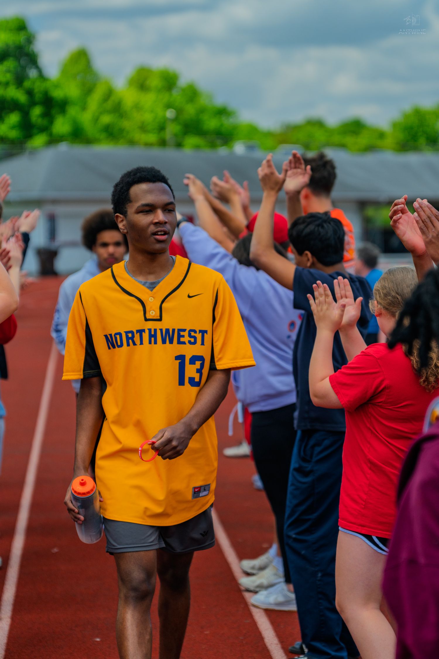 Athlete in Northwest #13 yellow jersey walks track while teammates give high-fives during a school sports event.